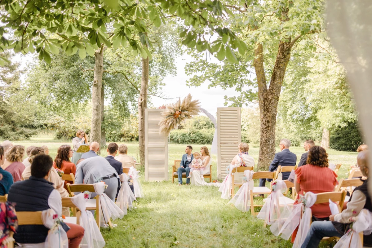 Cérémonie de mariage laïque en plein air avec invités assis face à l'arche nuptiale sous les arbres