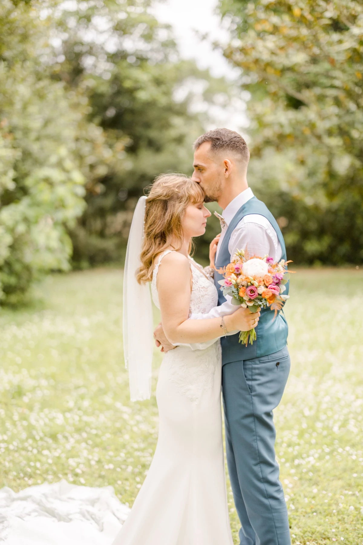 Couple de mariés s'embrassant dans un jardin verdoyant, la mariée tenant un bouquet coloré