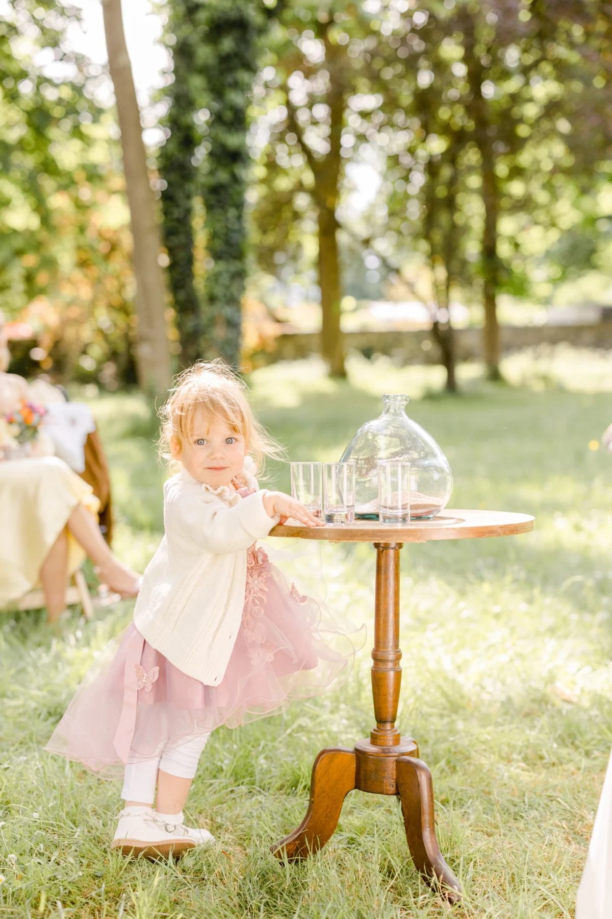 Petite fille en robe rose et blanche près d'une table en bois lors d'une cérémonie de mariage en plein air