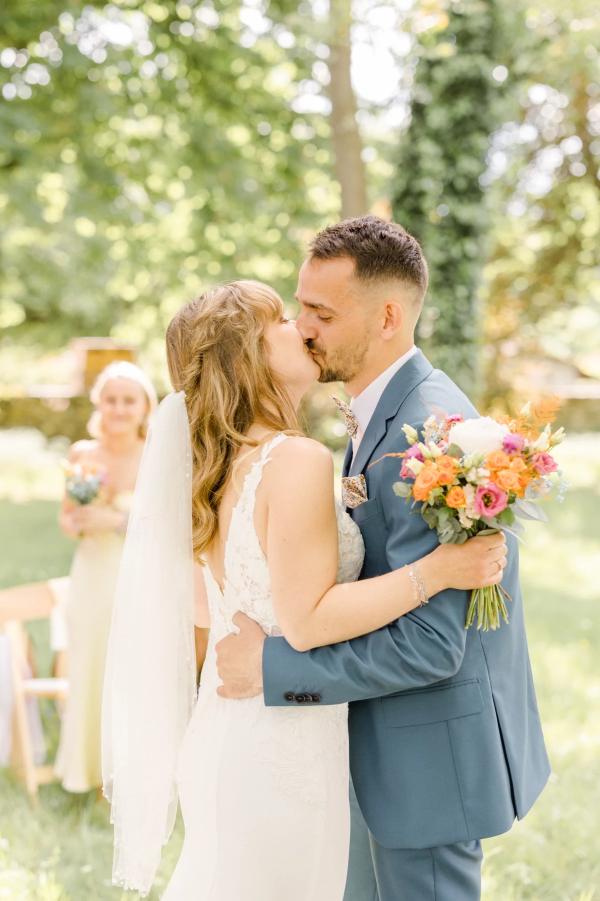 Couple de mariés s'embrassant lors de leur cérémonie laïque en plein air, bouquet coloré à la main