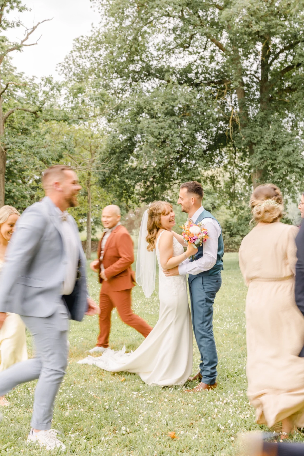 Mariés enlacés dans un jardin verdoyant entourés d'invités en mouvement lors d'une cérémonie extérieure