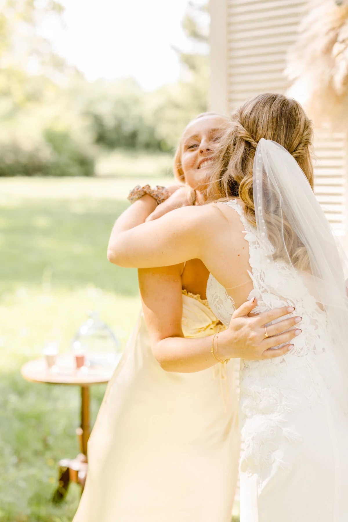 Mariée en robe blanche avec voile enlace tendrement sa demoiselle d'honneur en robe jaune lors d'un mariage