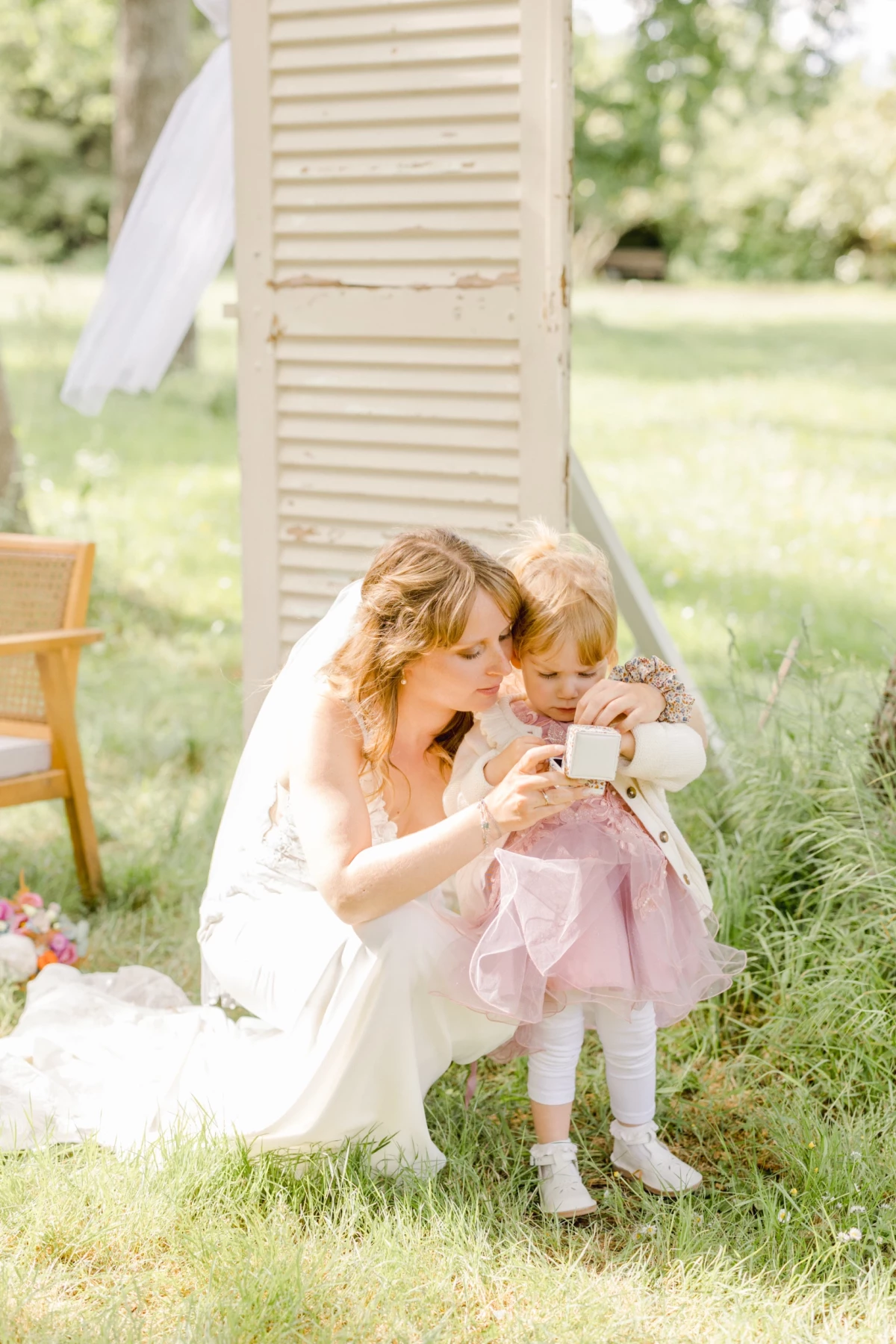 Mariée en robe blanche partageant un moment tendre avec une petite fille en rose dans un jardin