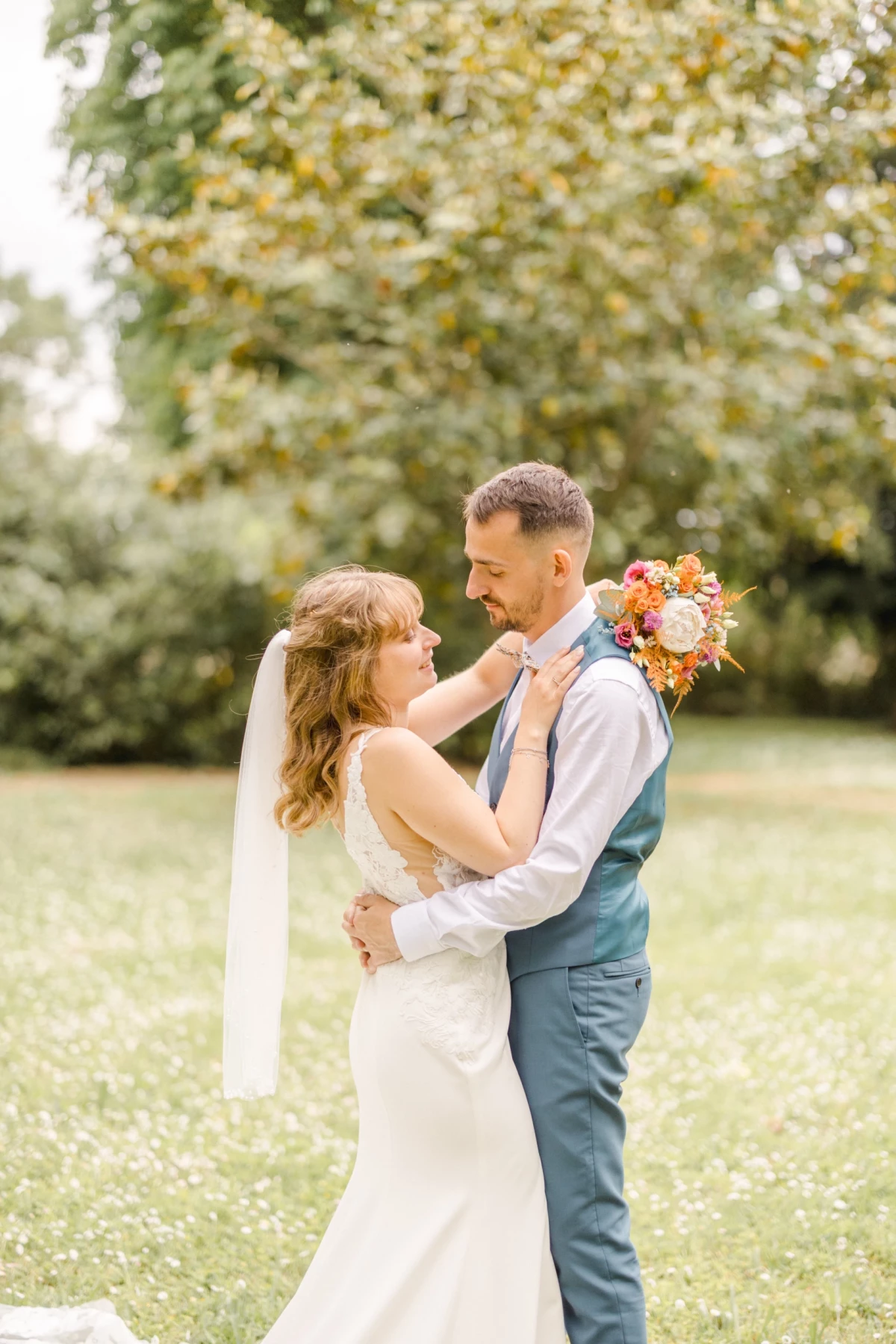 Couple de mariés s'enlaçant tendrement dans un jardin verdoyant sous un arbre lumineux
