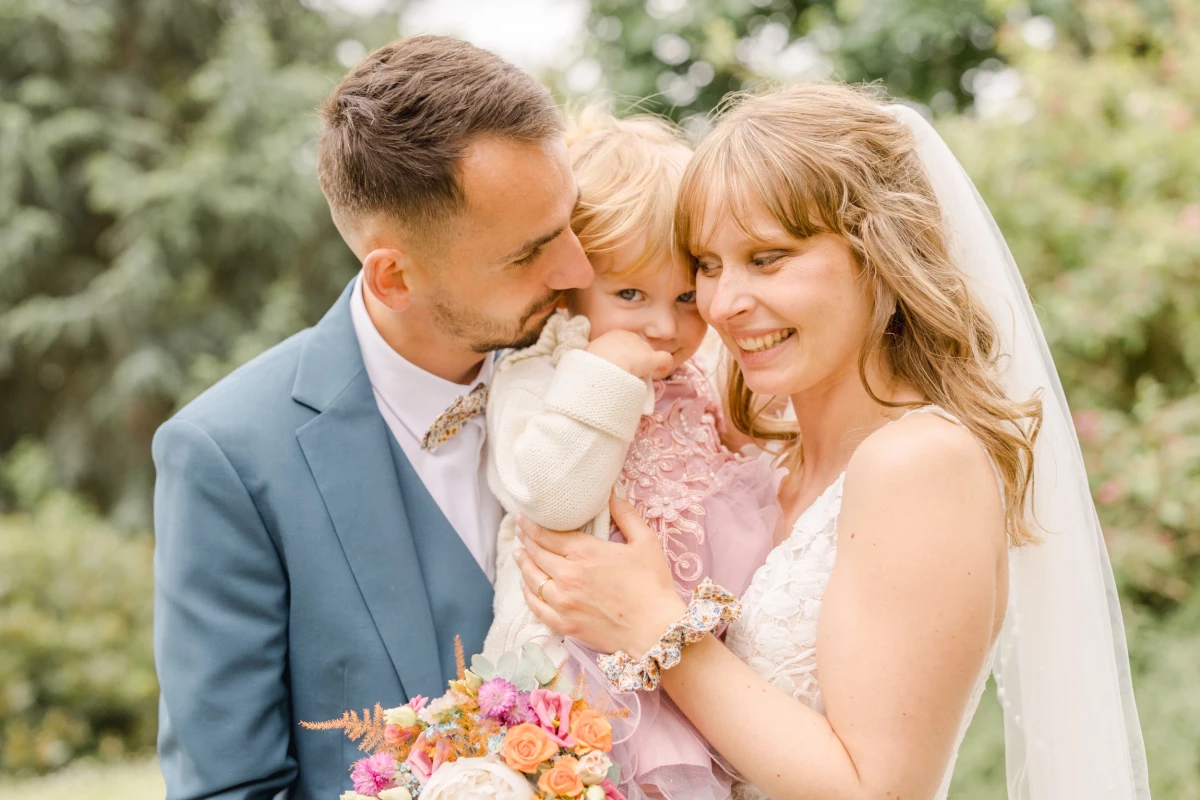 Couple de mariés enlace leur petite fille en robe rose lors d'un mariage en extérieur lumineux