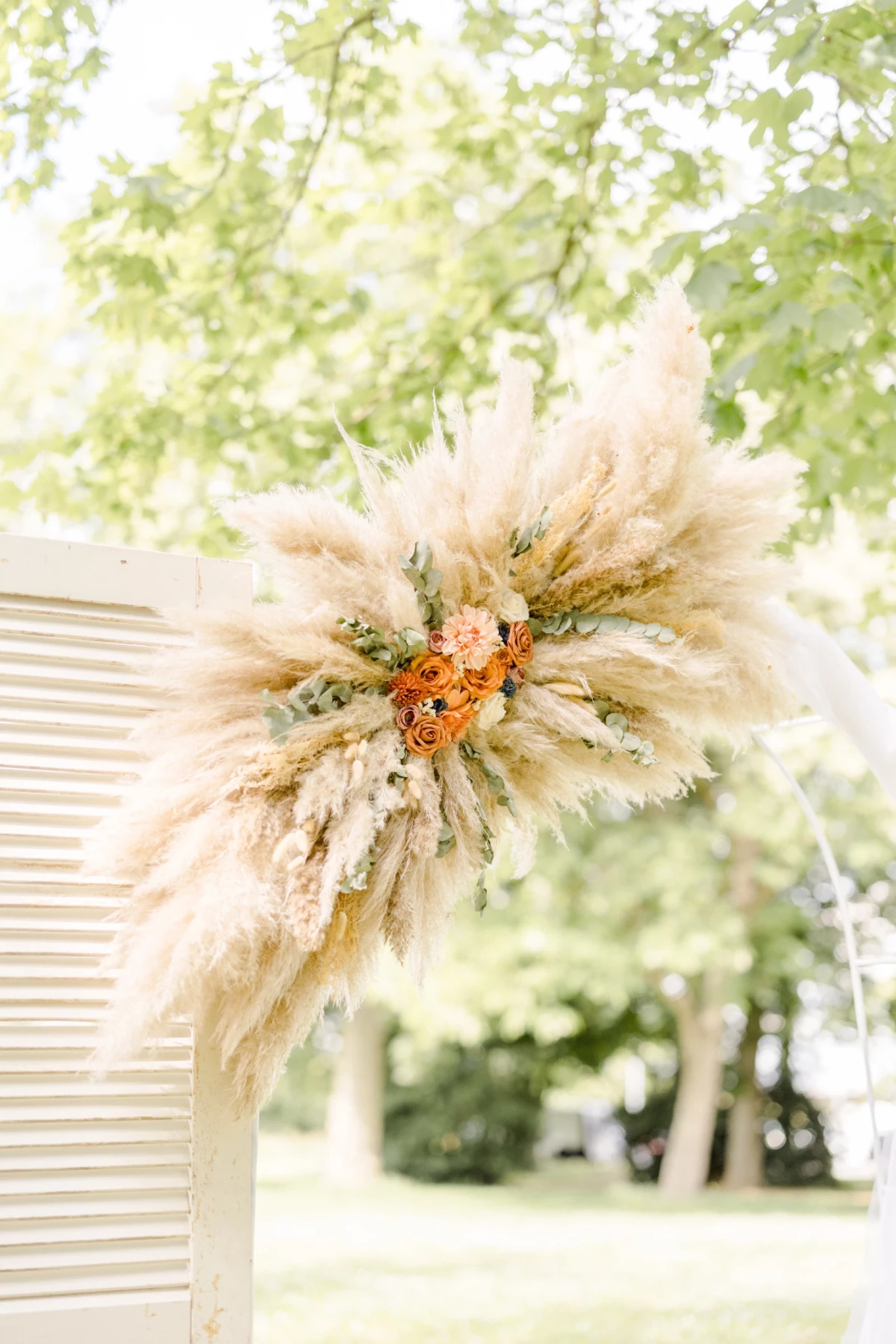 Couronne florale de pampa beige et fleurs orangées suspendue pour décoration de cérémonie champêtre