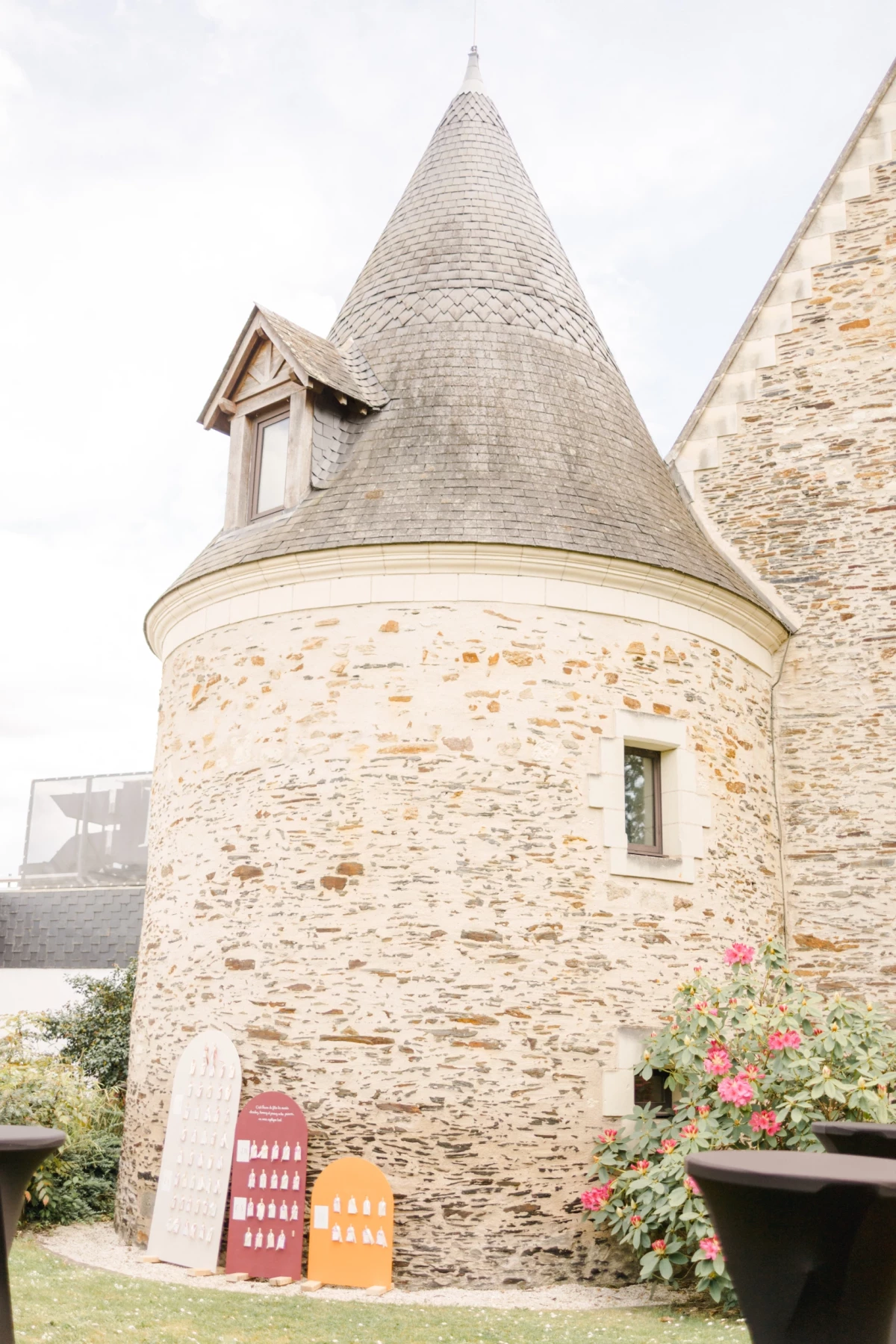Tour ronde en pierre d'un château avec toit conique en ardoise et rosiers grimpants roses au premier plan