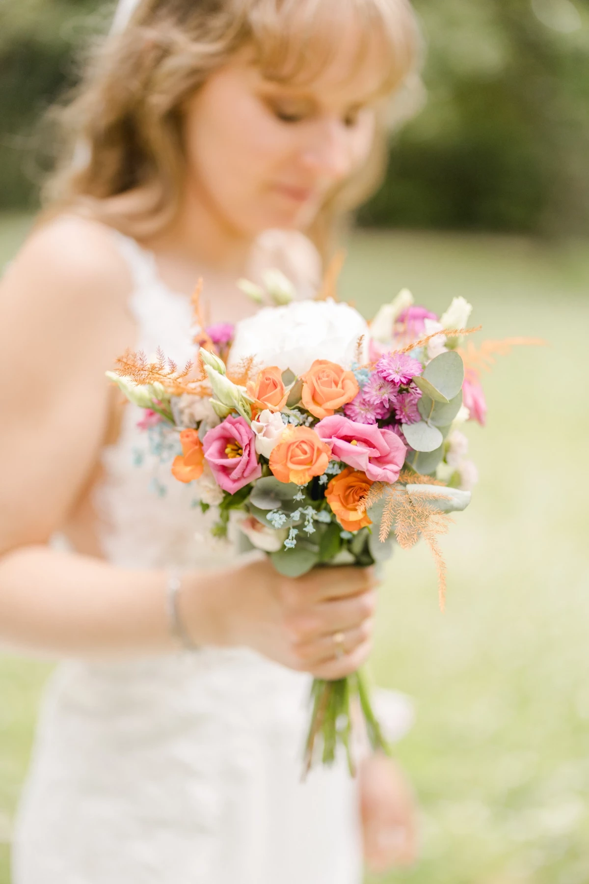 Mariée tenant un bouquet de fleurs coloré aux tons oranges, roses et blancs en extérieur