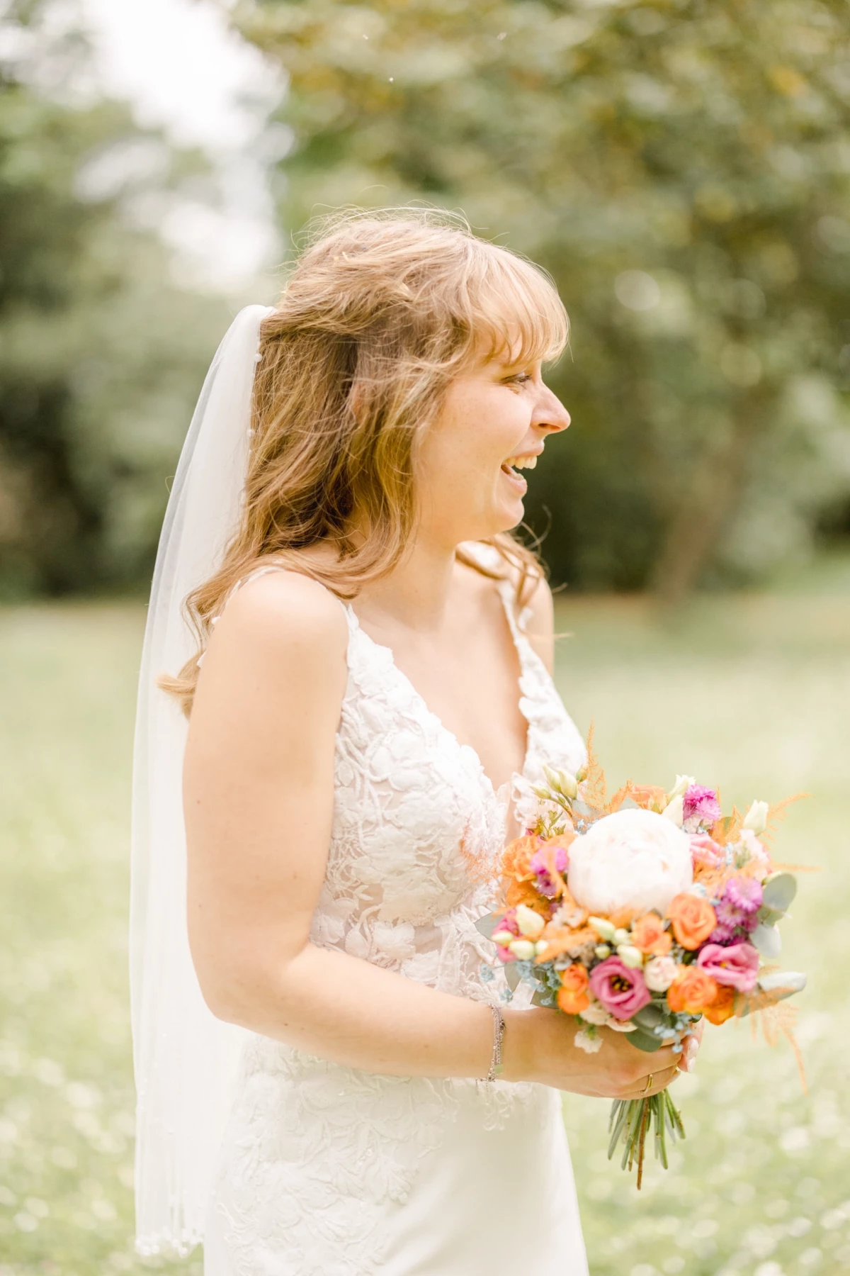 Mariée souriante en robe blanche tenant un bouquet coloré dans un jardin verdoyant