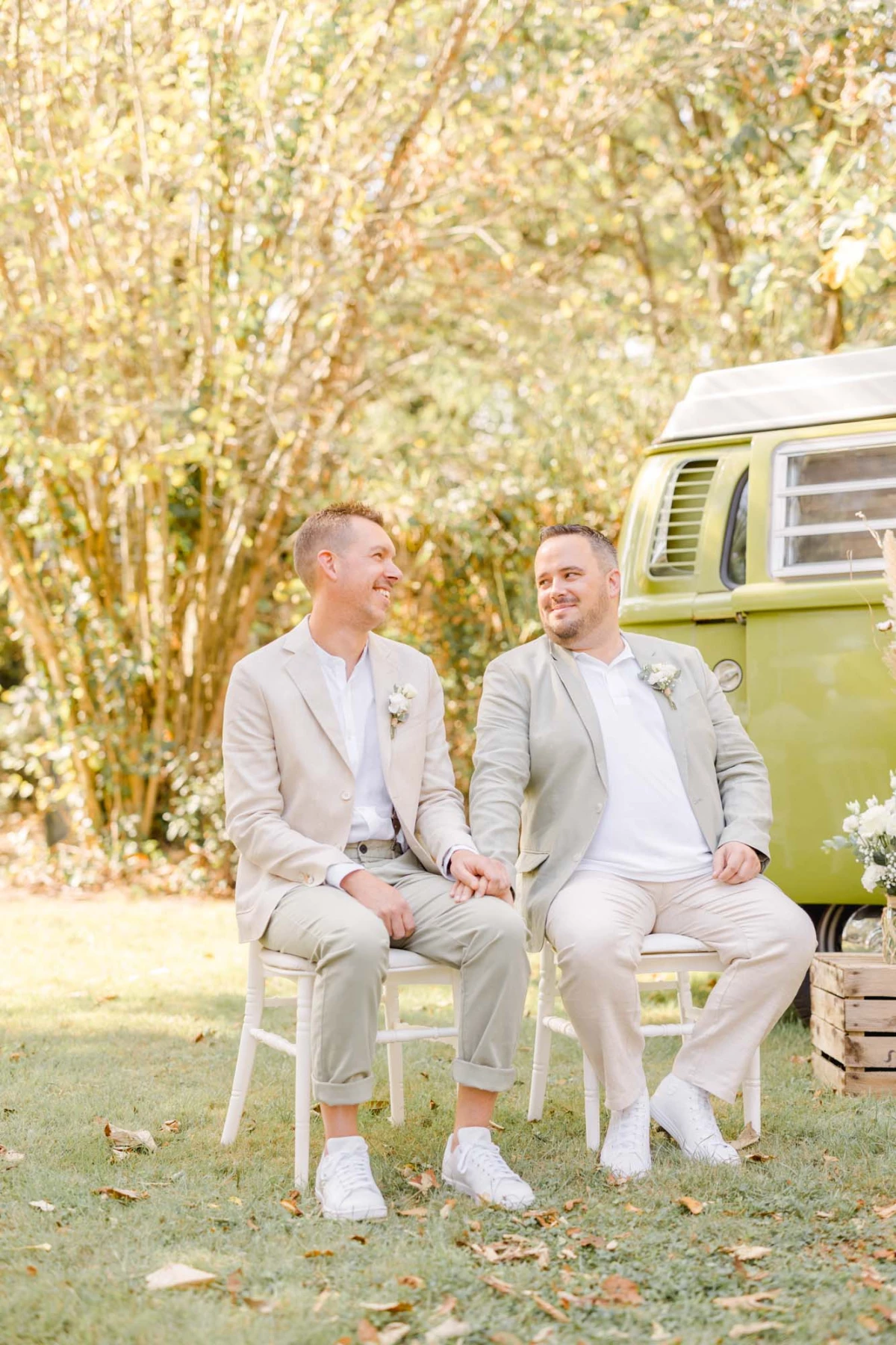 Séance mariage extérieur : deux mariés en costume beige échangent un regard complice assis devant un van vintage vert