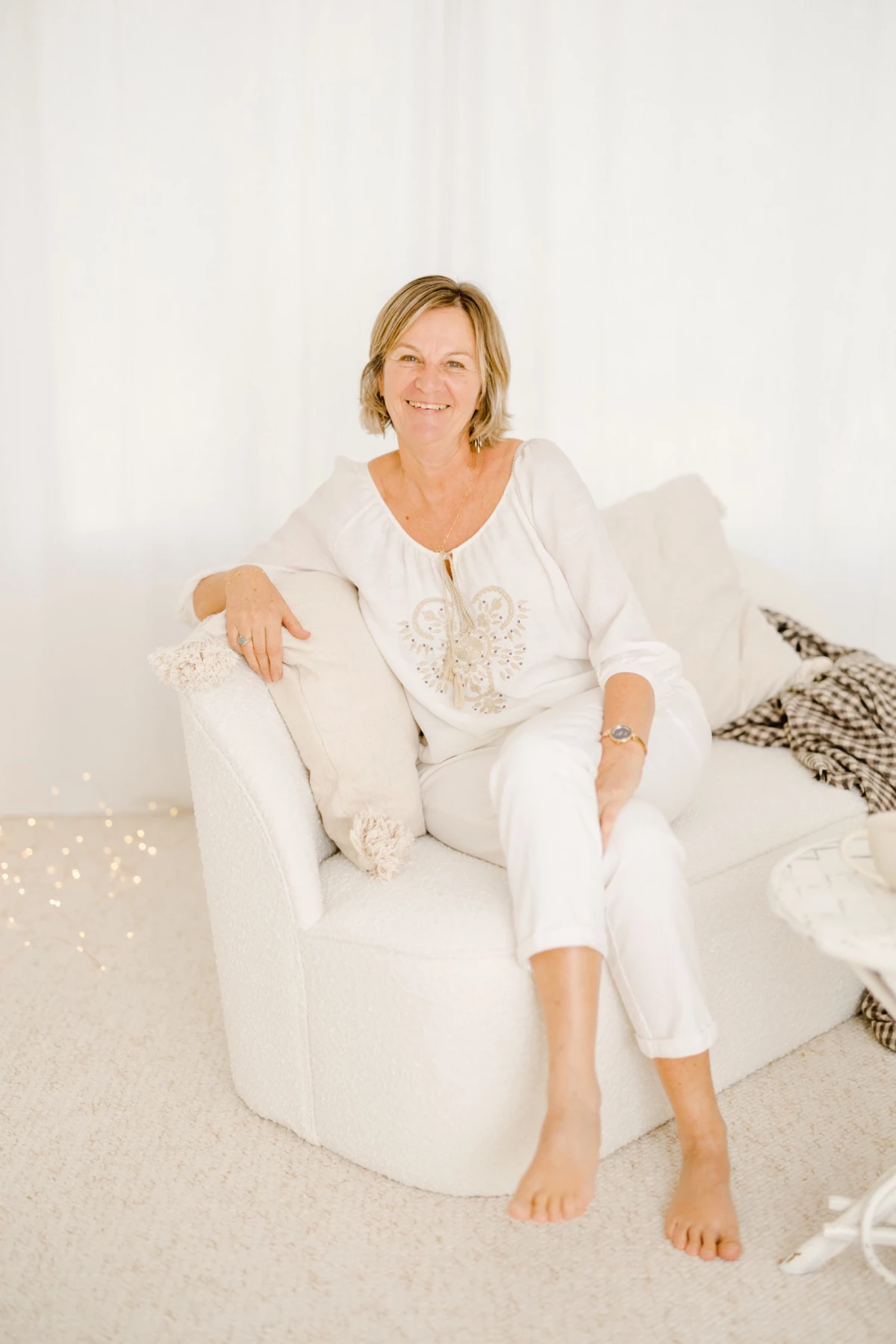 Femme souriante en tenue blanche assise dans un fauteuil blanc, portrait studio lumineux et épuré
