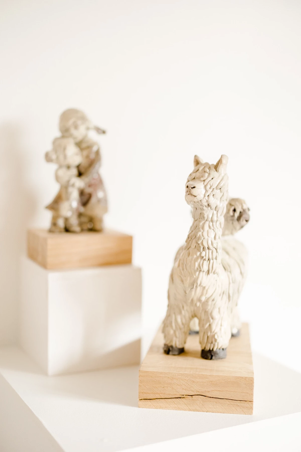 Portrait corporate artisan céramiste : sculptures d'alpagas en céramique blanche sur socles bois dans un atelier lumineux
