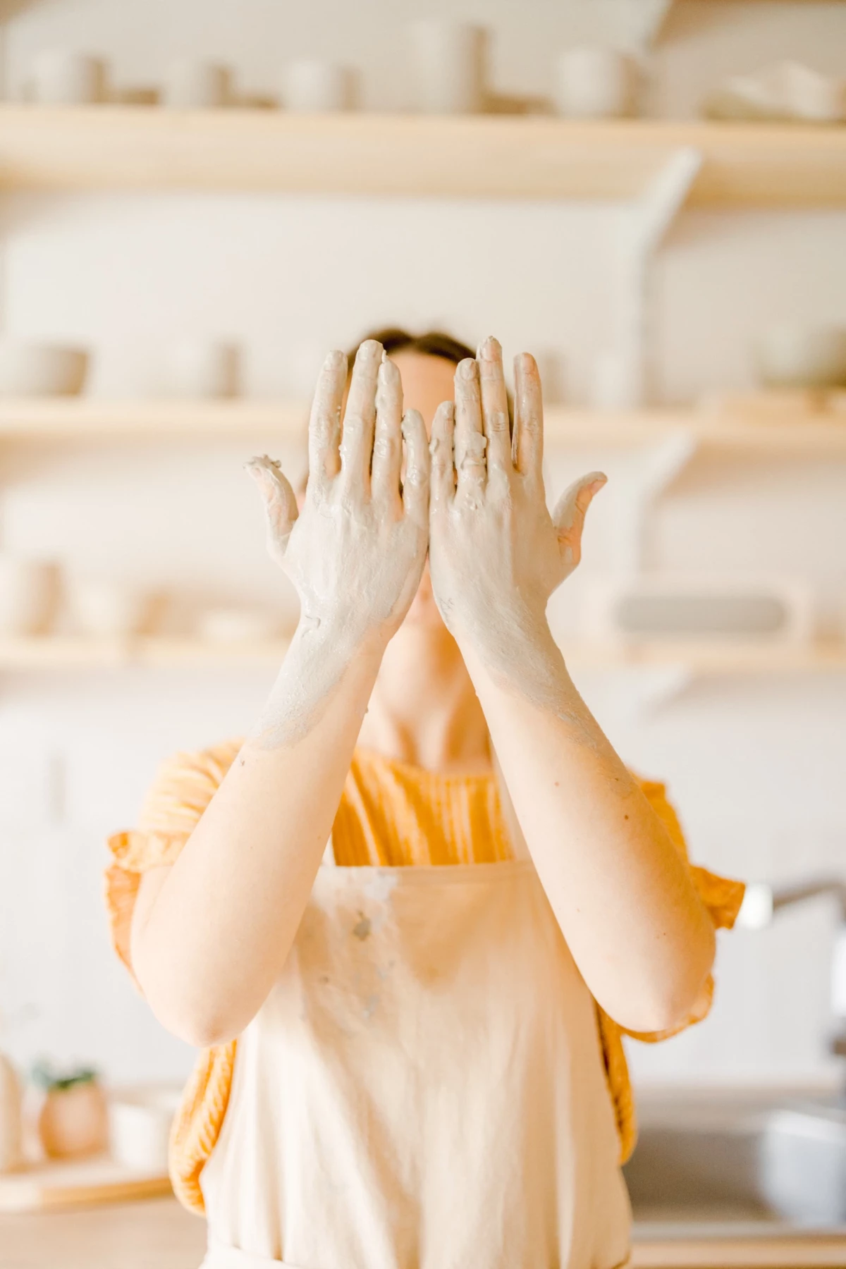 Portrait corporate artisan céramiste : geste créatif des mains dans un atelier lumineux aux tons beige et orange, authenticité du savoir-faire