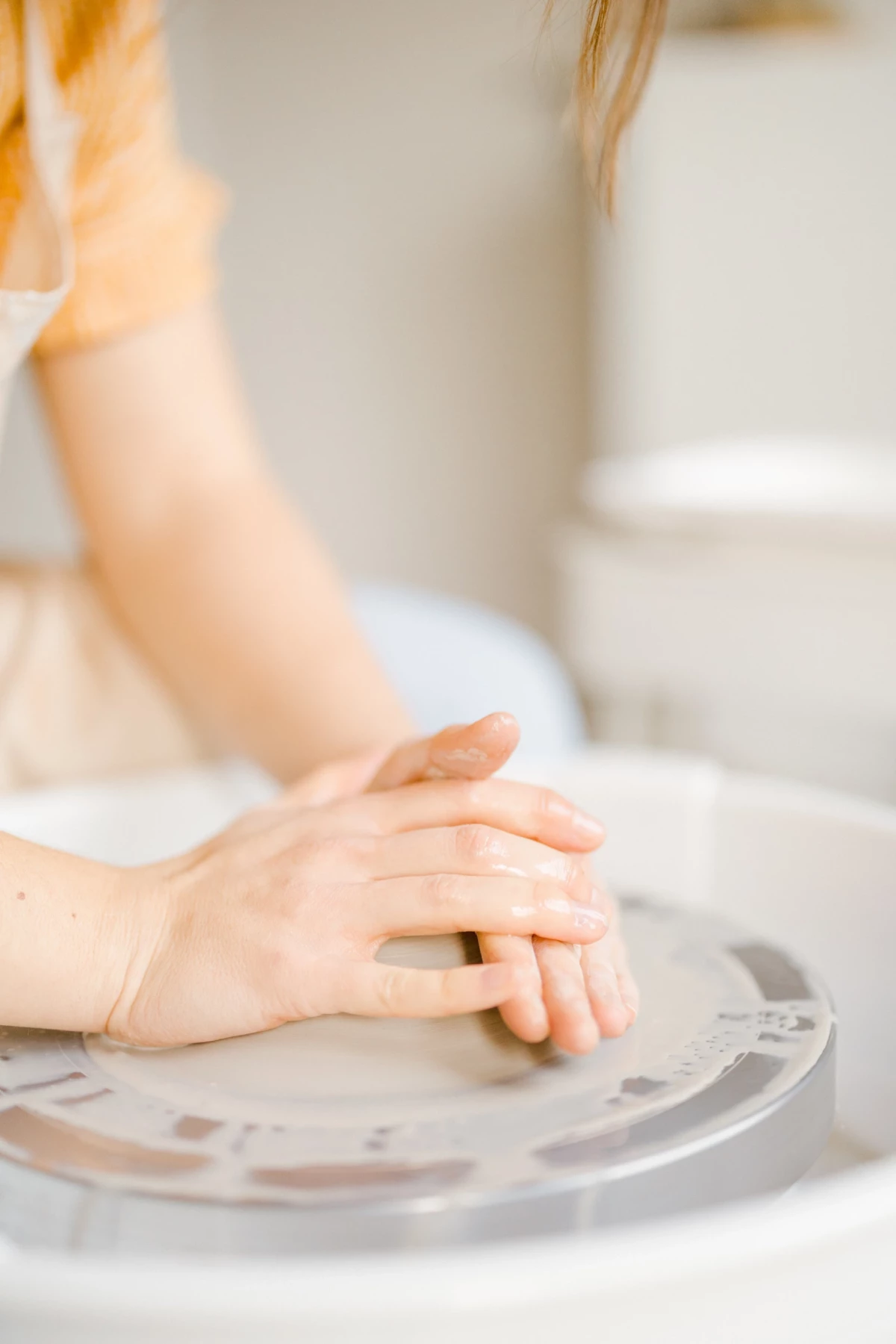 Portrait corporate en atelier : mains délicates d'artiste céramiste modelant l'argile sur un tour, gestes précis et créatifs