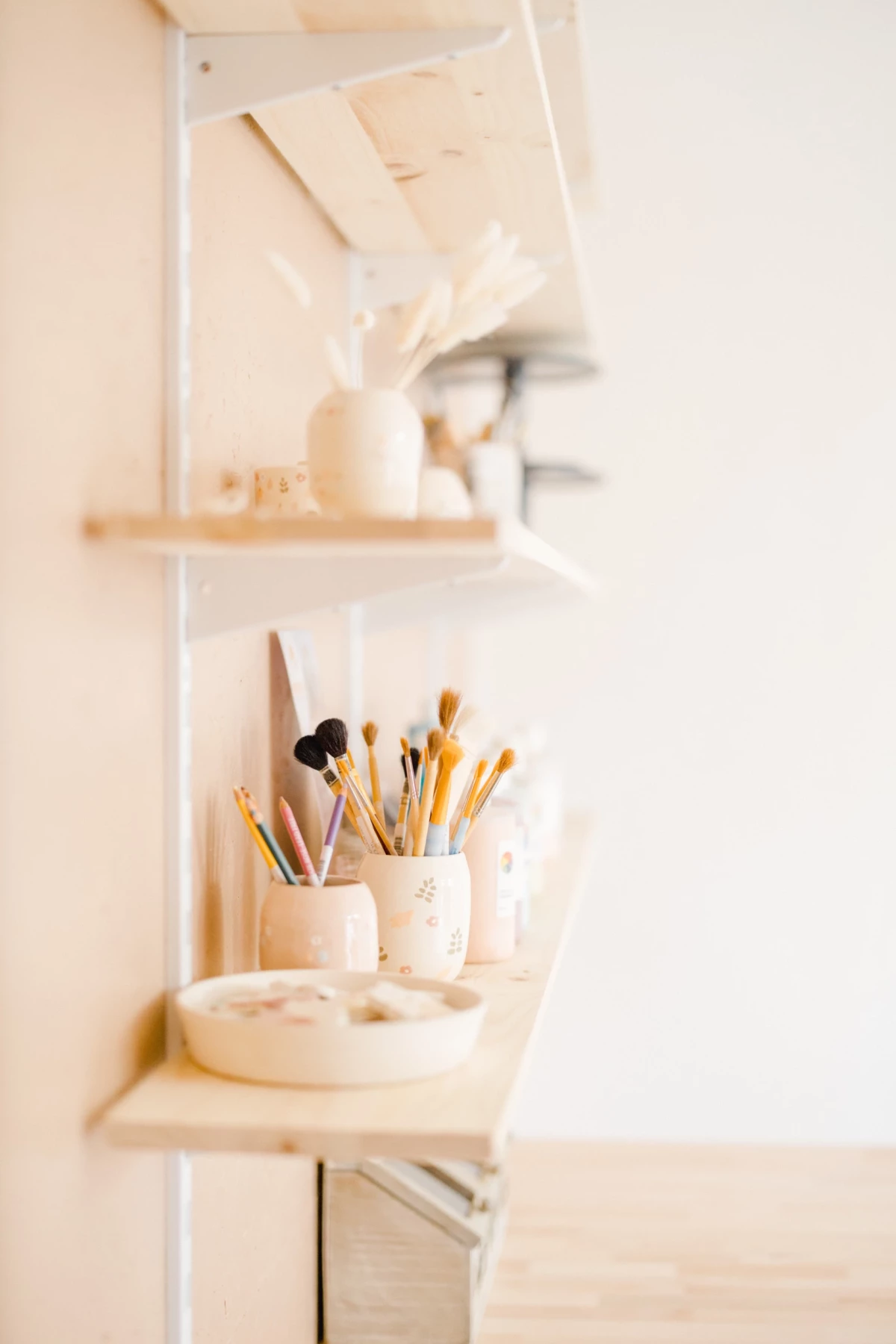 Portrait corporate en studio : étagère d'atelier céramiste avec pinceaux aquarelle et décoration naturelle, lumière douce et beige