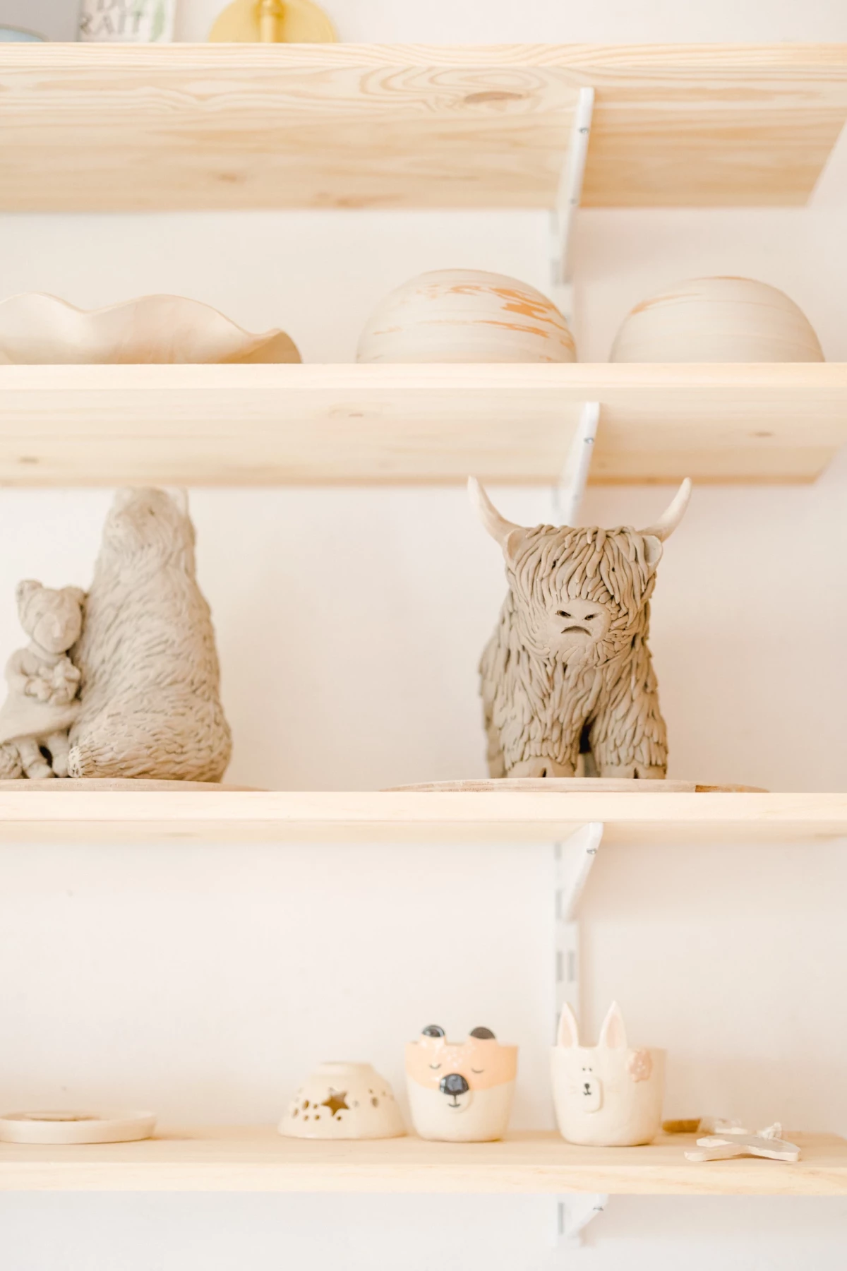 Portrait corporate dans l'atelier d'une céramiste : étagères en bois clair exposant créations artisanales, ambiance naturelle