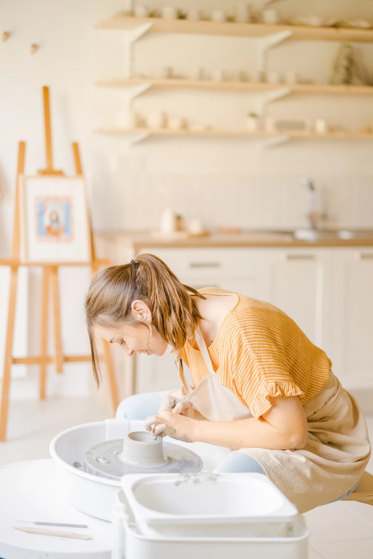 Portrait corporate artisan : céramiste façonne une pièce au tour de potier dans son atelier lumineux à la lumière naturelle