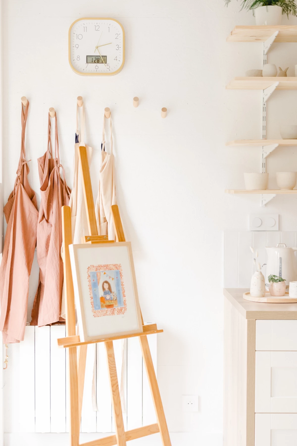 Portrait corporate dans atelier céramiste : espace créatif lumineux aux tons beiges, chevalet et étagères en bois, ambiance artisanale douce