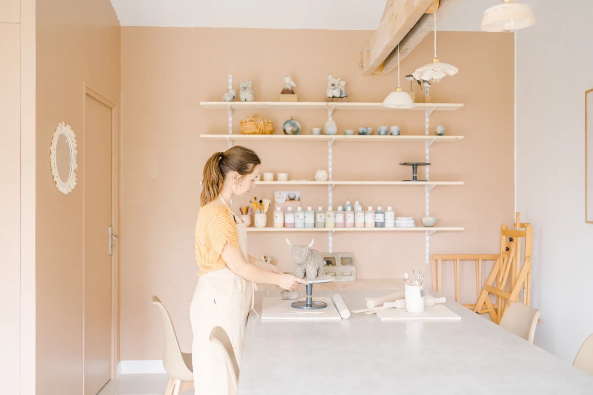 Portrait corporate dans un atelier de céramiste : artisane au travail devant ses créations, ambiance lumineuse et épurée en Vendée