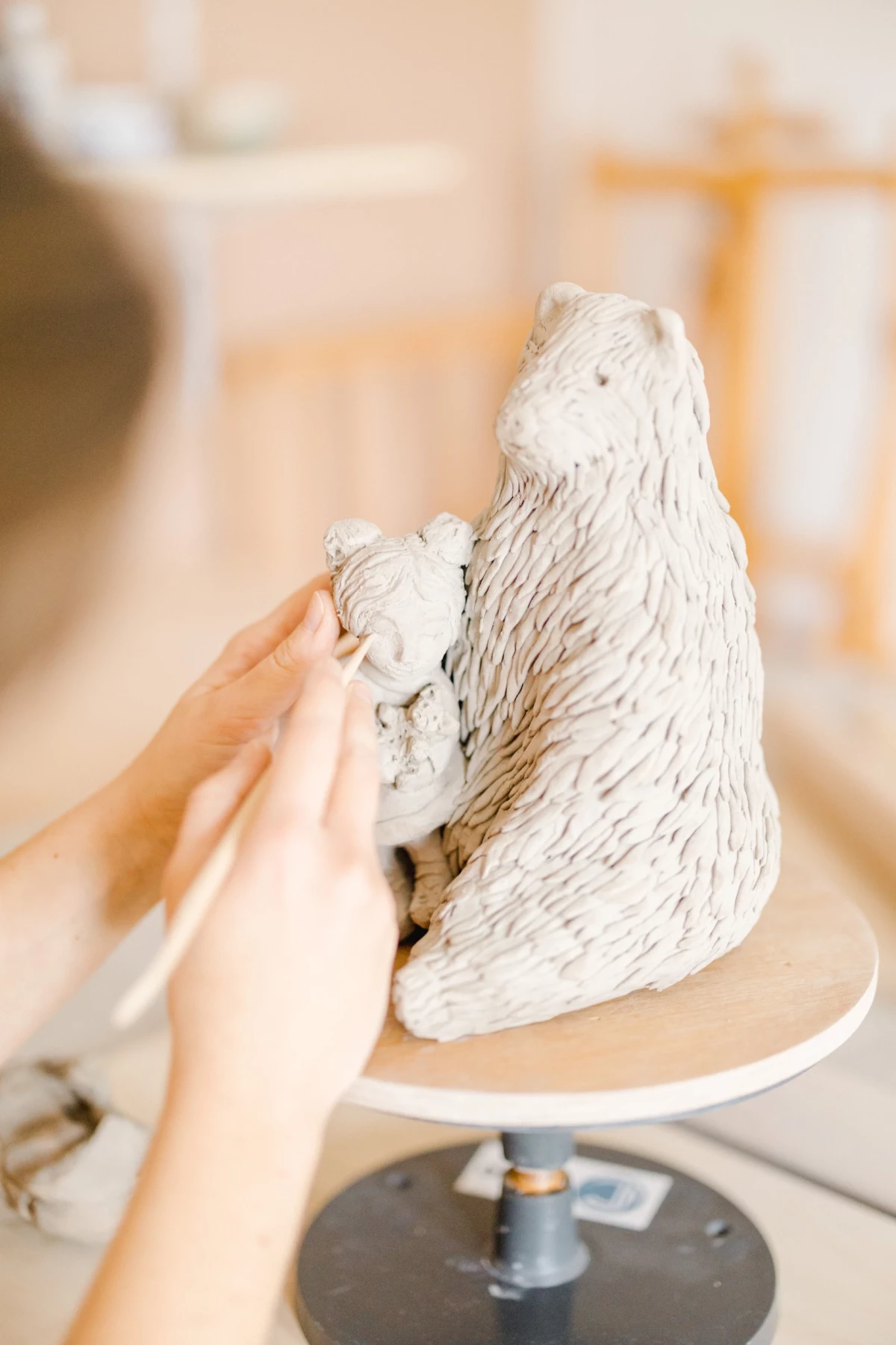 Portrait corporate en atelier céramique : mains d'artiste façonnant une sculpture animalière blanche, geste délicat et précis