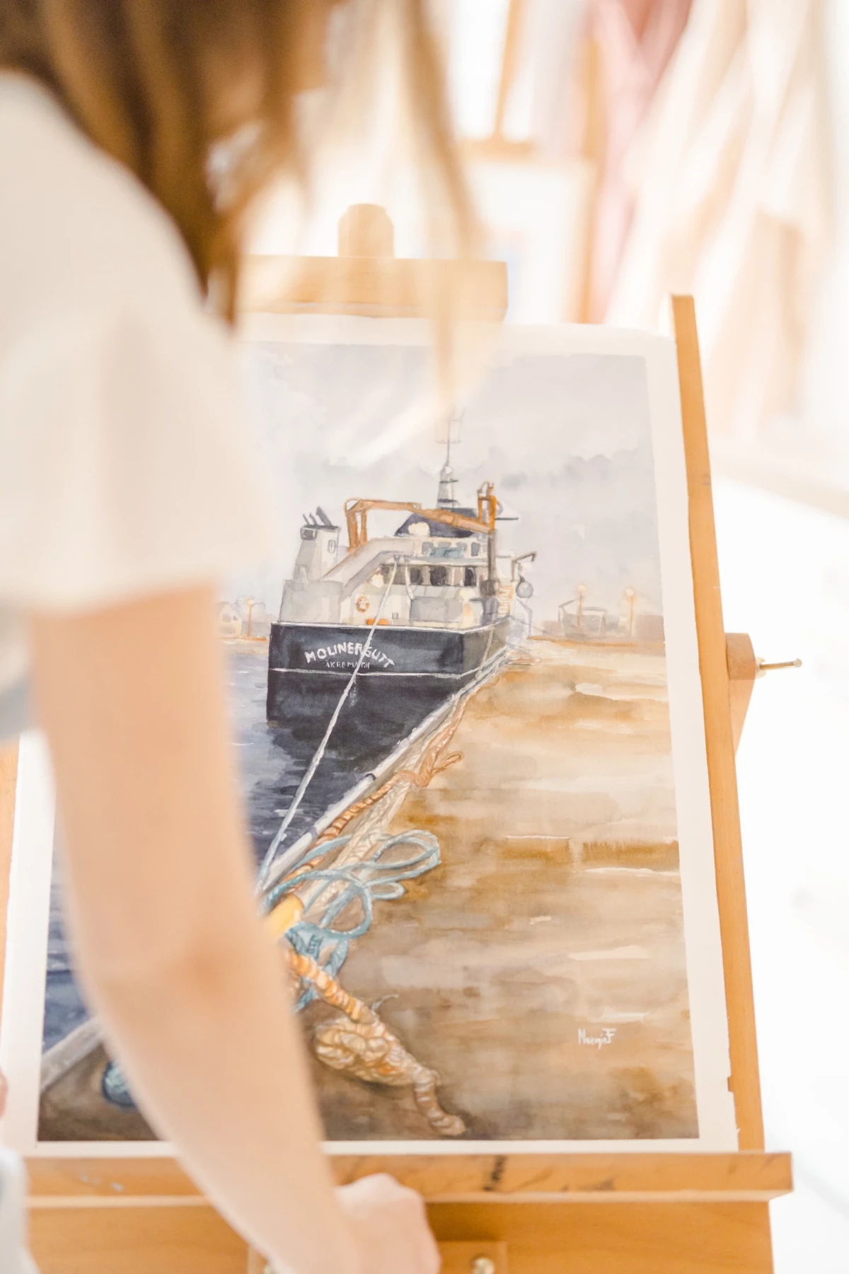 Portrait corporate d'une aquarelliste à l'œuvre dans son atelier en Vendée, peignant un bateau amarré dans des tons beige et bleu