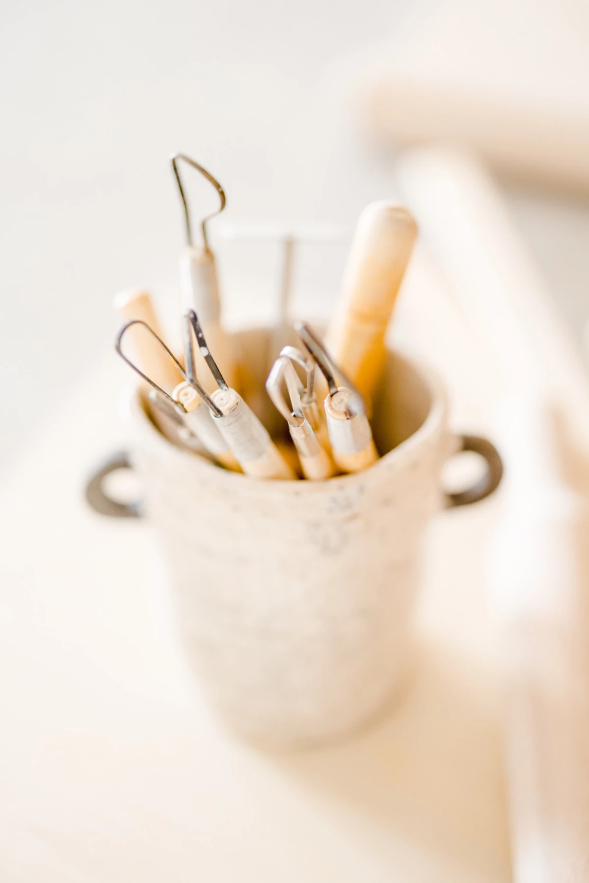 Séance corporate au studio : outils d'artiste céramiste et aquarelliste dans un pot en grès beige, ambiance artisanale et douce