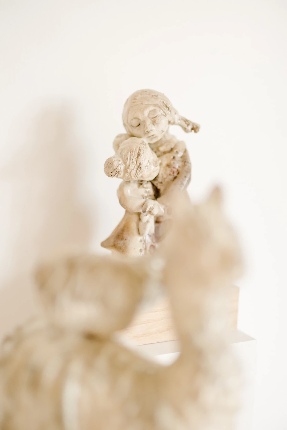 Artisan céramiste en Vendée : figurine en céramique beige représentant un ange avec enfant, lumière douce et fond neutre