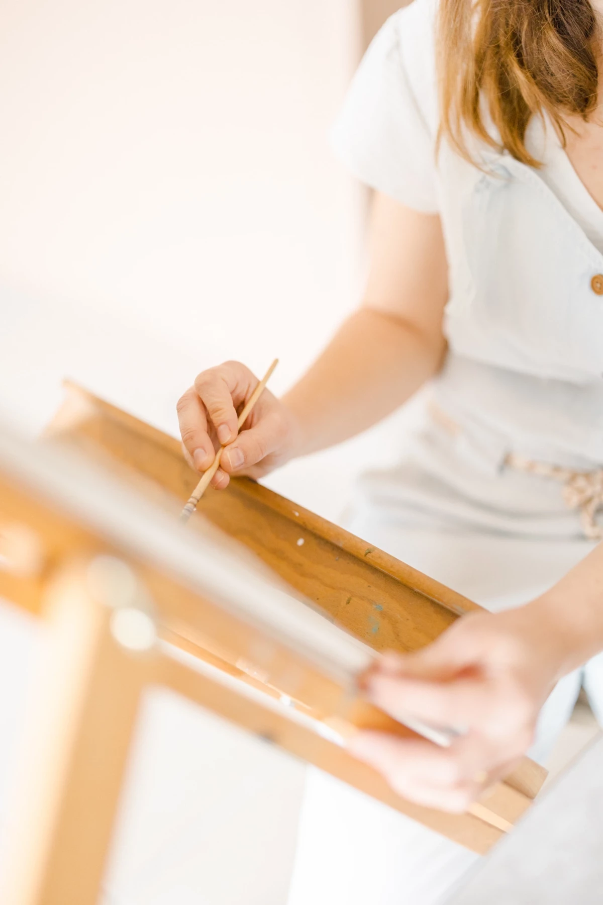 Portrait corporate artisan : mains d'une céramiste marquant une pièce en bois dans son atelier, geste précis et créatif