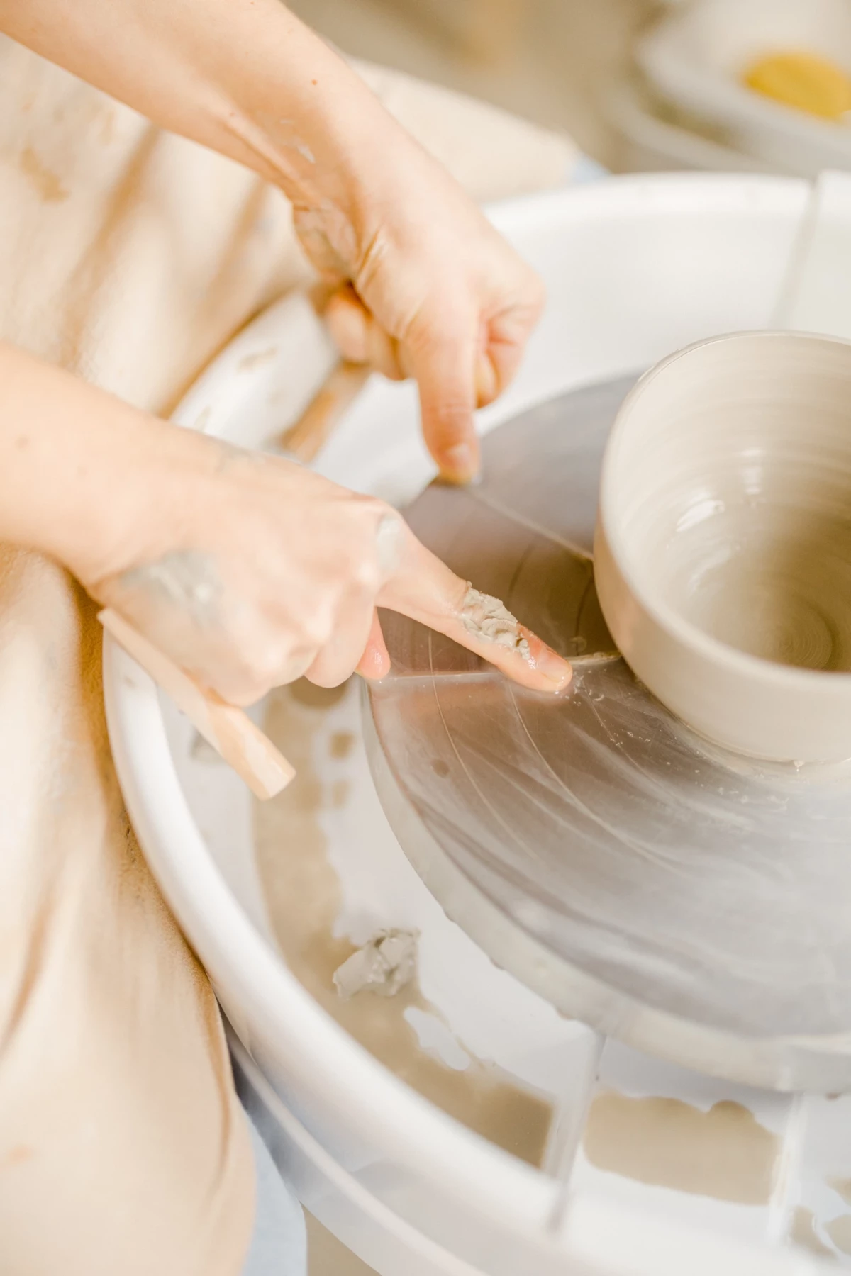 Portrait corporate en atelier : mains d'artisan céramiste sculptant de l'argile sur un tour de potier, gestes précis et professionnels
