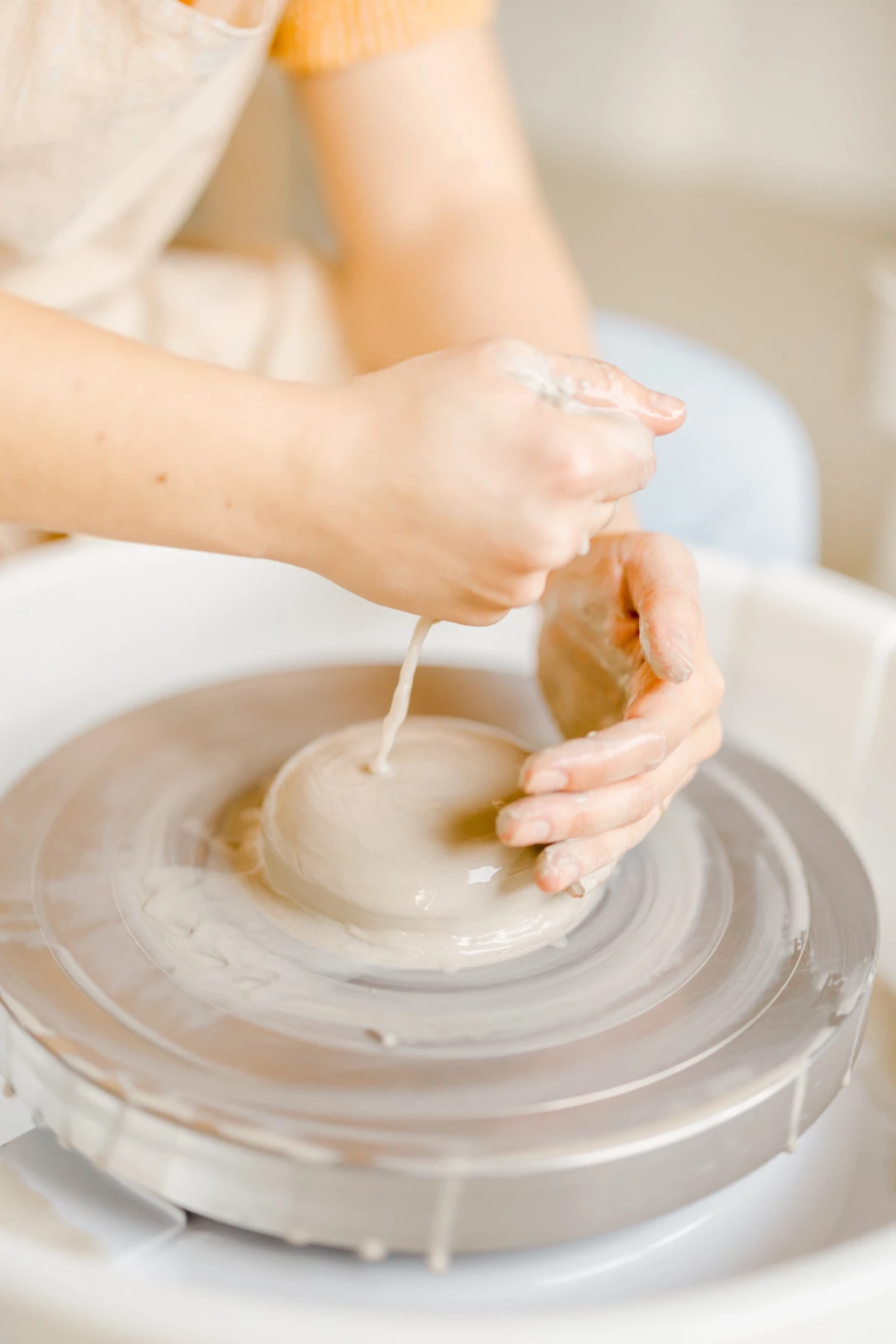 Portrait corporate en atelier : mains d'artisan modelant une pièce de céramique sur tour de potier, geste précis et créatif