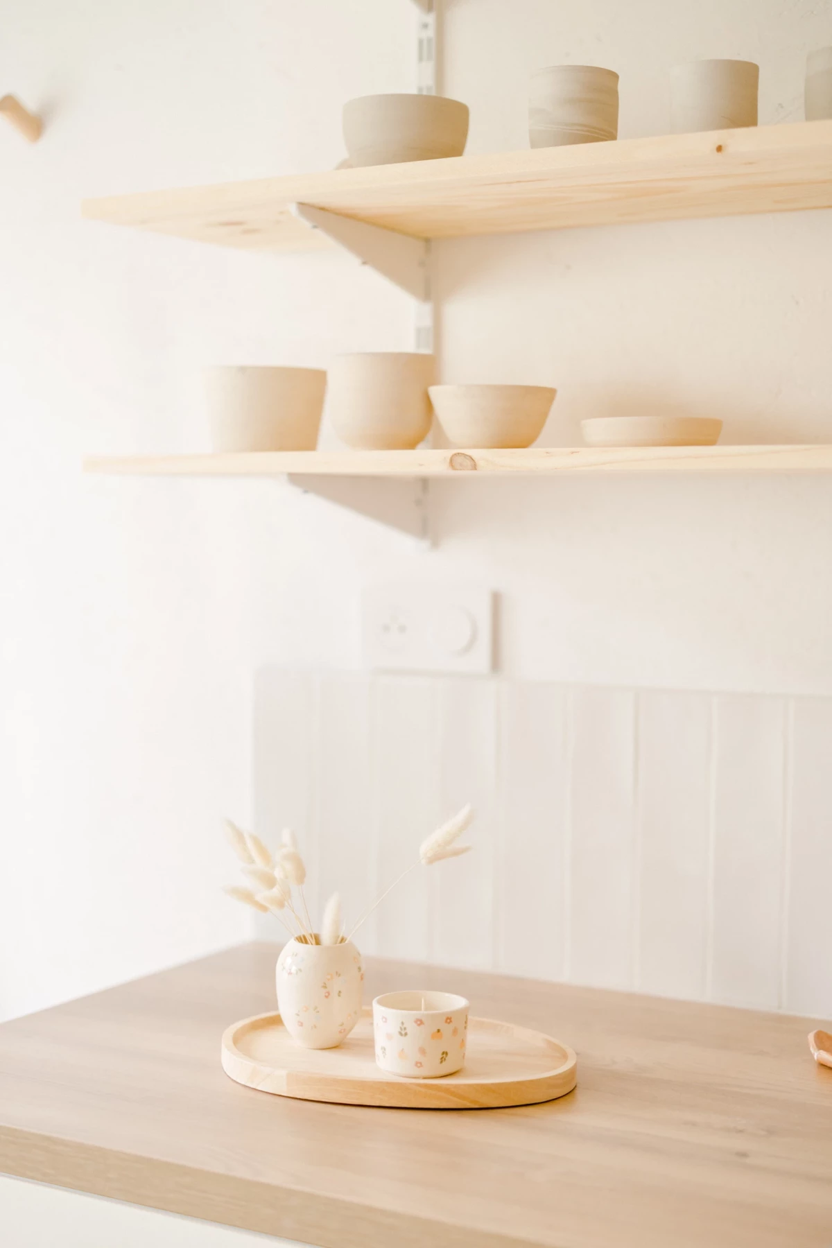 Photographie corporate atelier céramiste : vaisselle artisanale beige sur étagères bois, ambiance douce et épurée