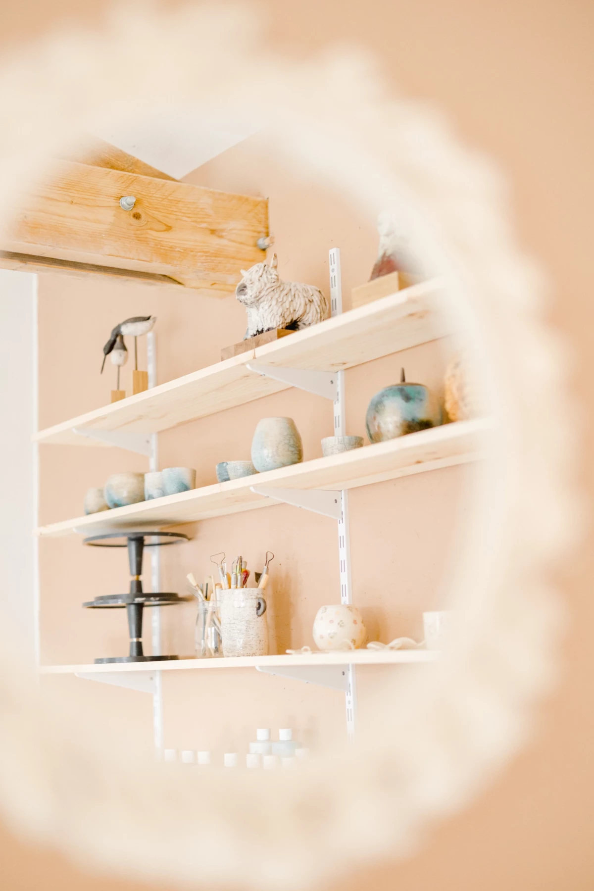 Portrait corporate artisan céramiste : étagères d'atelier avec créations en tons beige et bleu, ambiance douce et lumineuse en Vendée