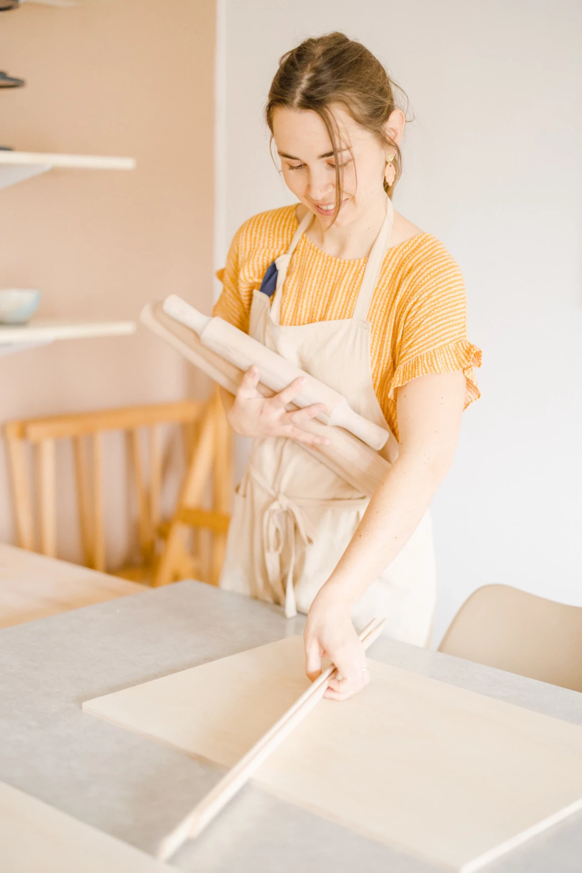 Portrait corporate d'une céramiste dans son atelier, consultant un cahier avec concentration, lumière naturelle douce