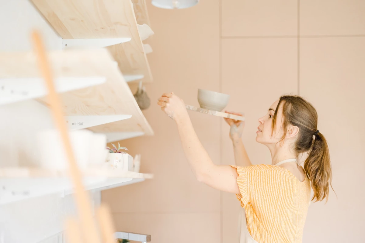 Portrait corporate : artisane céramiste organise ses créations dans son atelier lumineux aux tons blanc et beige