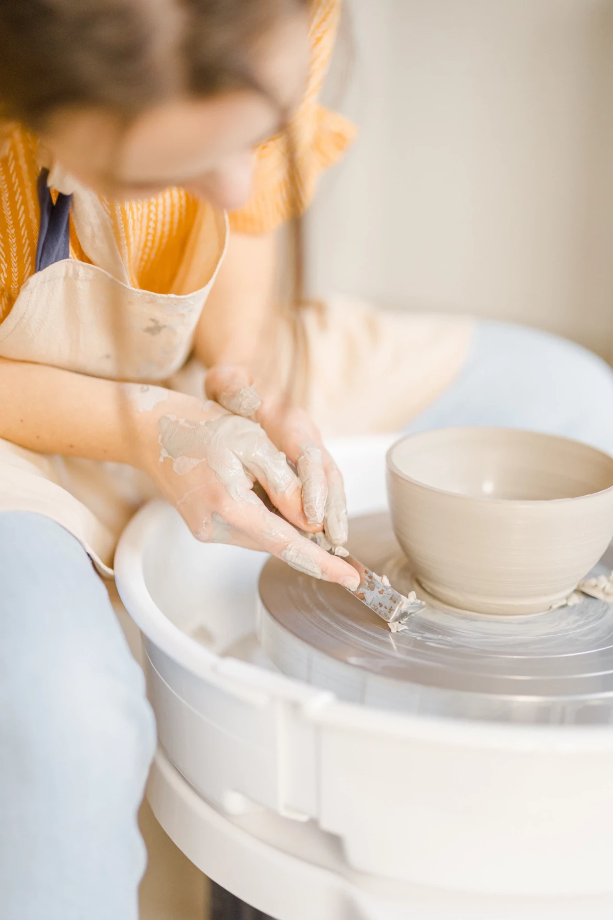 Portrait professionnel d'une céramiste en atelier : mains délicates façonnent une pièce sur le tour, geste précis et concentration créative
