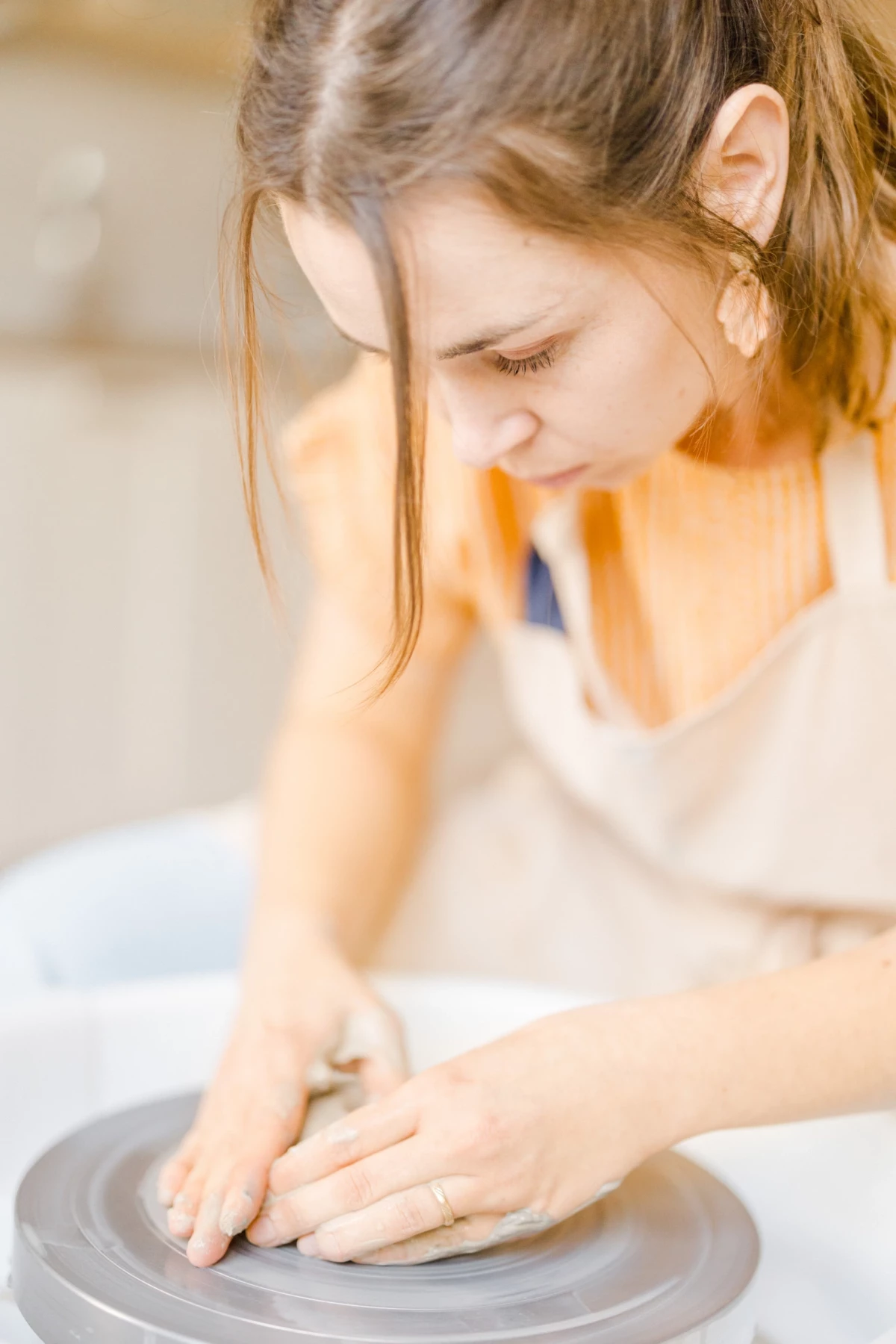 Portrait corporate artisan céramiste : femme concentrée façonne l'argile au tour dans son atelier, gestes précis et douceur.