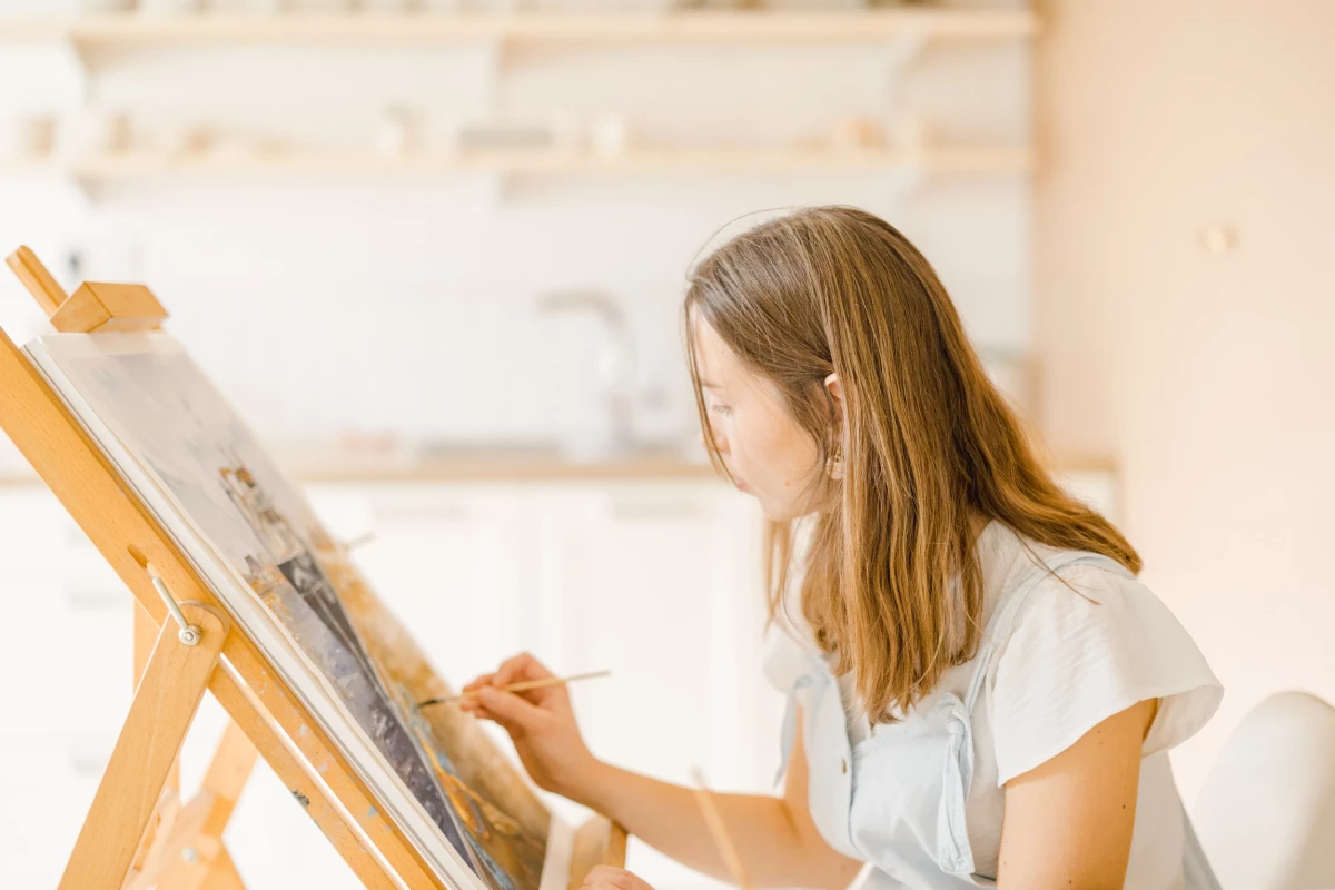 Portrait corporate atelier créatif : artiste aquarelliste peint sur chevalet dans son atelier lumineux, ambiance douce et professionnelle