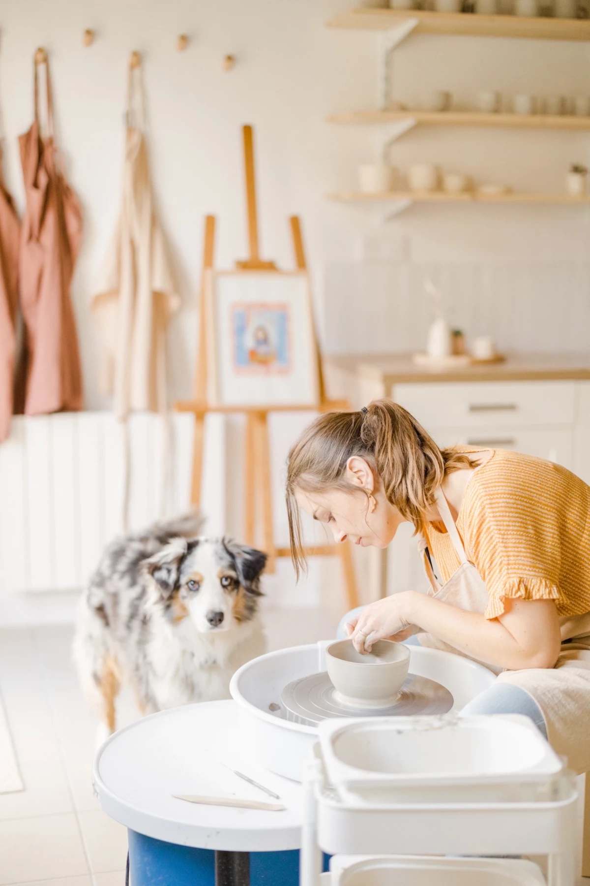 Portrait professionnel d'une céramiste aquarelliste dans son atelier lumineux, accompagnée de son chien, instant de complicité créative