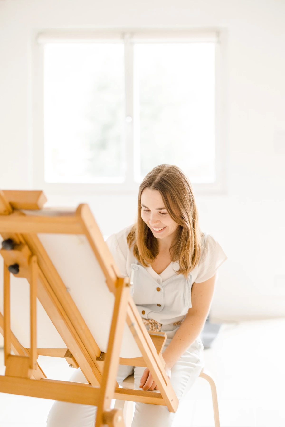 Portrait corporate d'une artisane céramiste dans son atelier lumineux, sourire authentique et concentration créative au travail