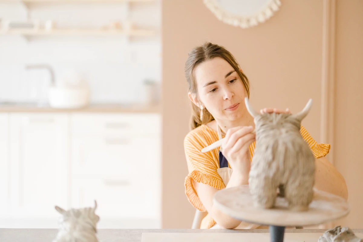 Portrait corporate atelier céramique : artisane sourit en caressant son chat gris, lumière douce et naturelle dans son atelier beige
