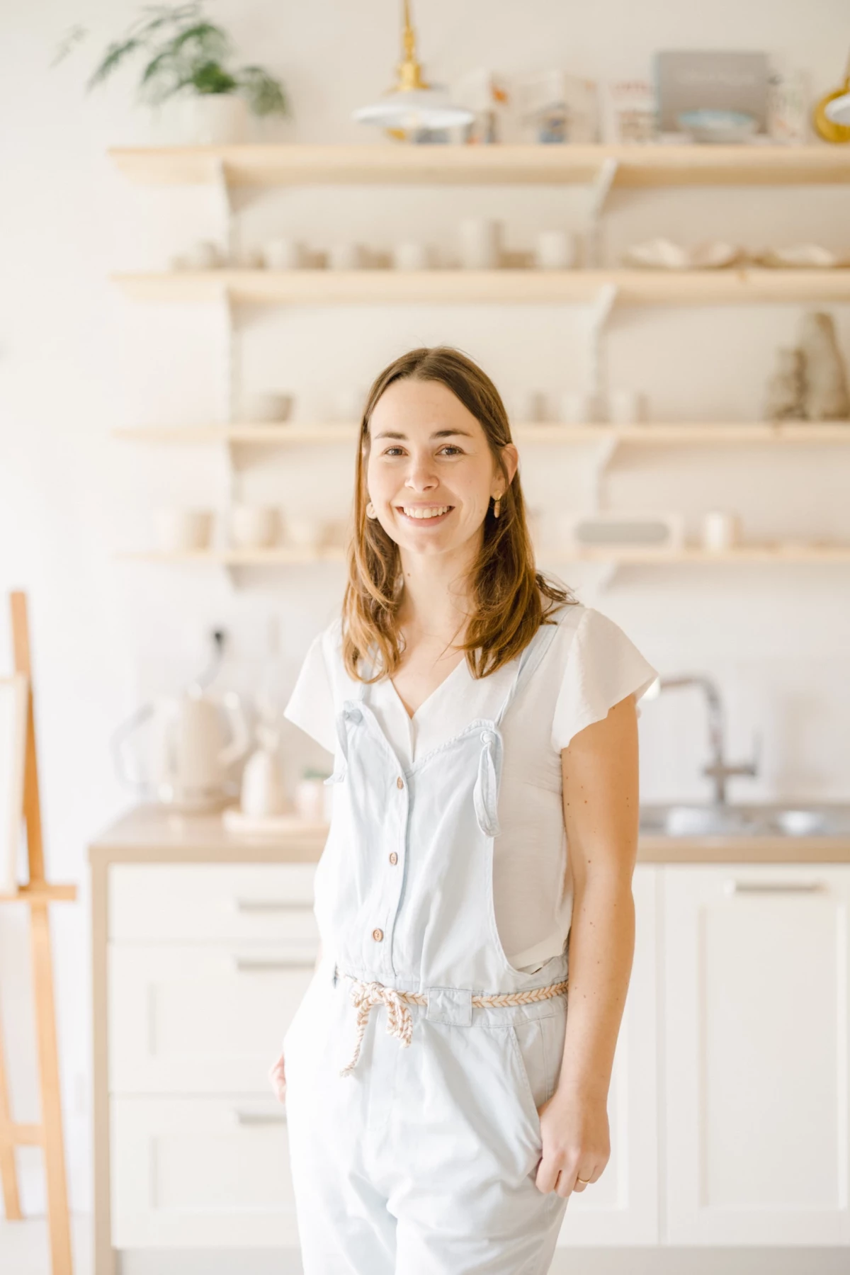 Portrait professionnel en studio : artisane céramiste souriante dans son atelier lumineux aux tons blancs et beiges