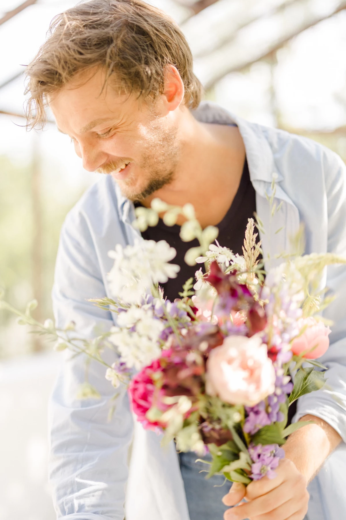 Portrait corporate d'un fleuriste artisan tenant un bouquet de fleurs printanier dans une verrière baignée de lumière douce