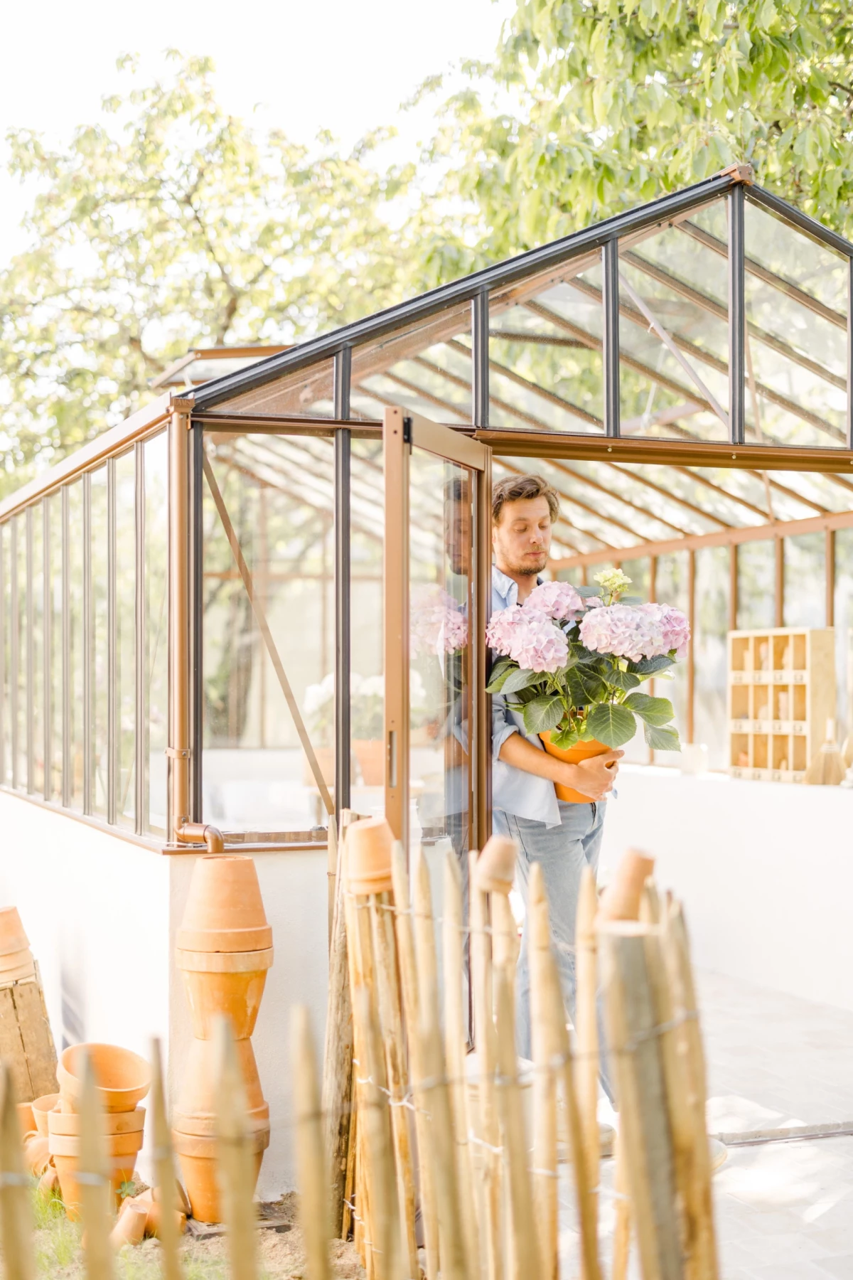 Portrait corporate fleuriste avec bouquet hortensia devant verrière métal, ambiance lumineuse et douce en extérieur Vendée