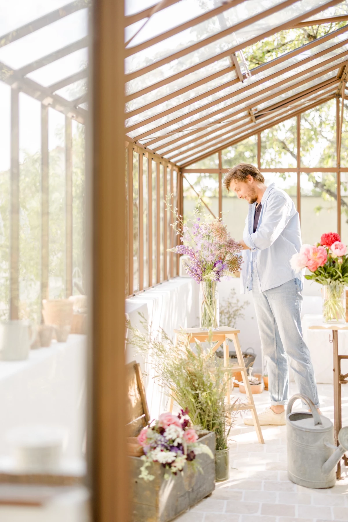 Portrait corporate fleuriste : artisan arrange un bouquet de fleurs printanier dans une verrière lumineuse aux tons doux et naturels
