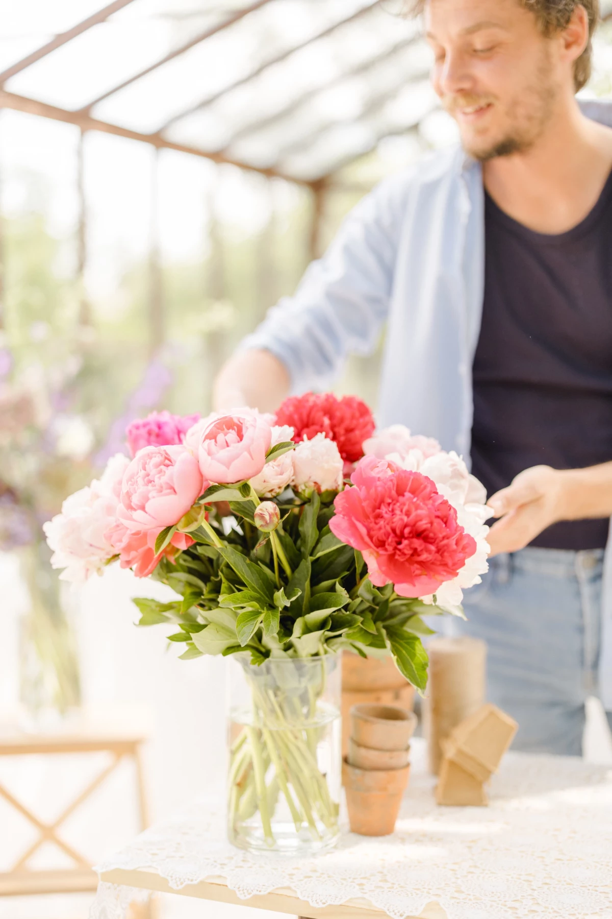 Séance corporate fleuriste : artisan compose un bouquet de pivoines roses sous verrière, ambiance douce et professionnelle en Vendée