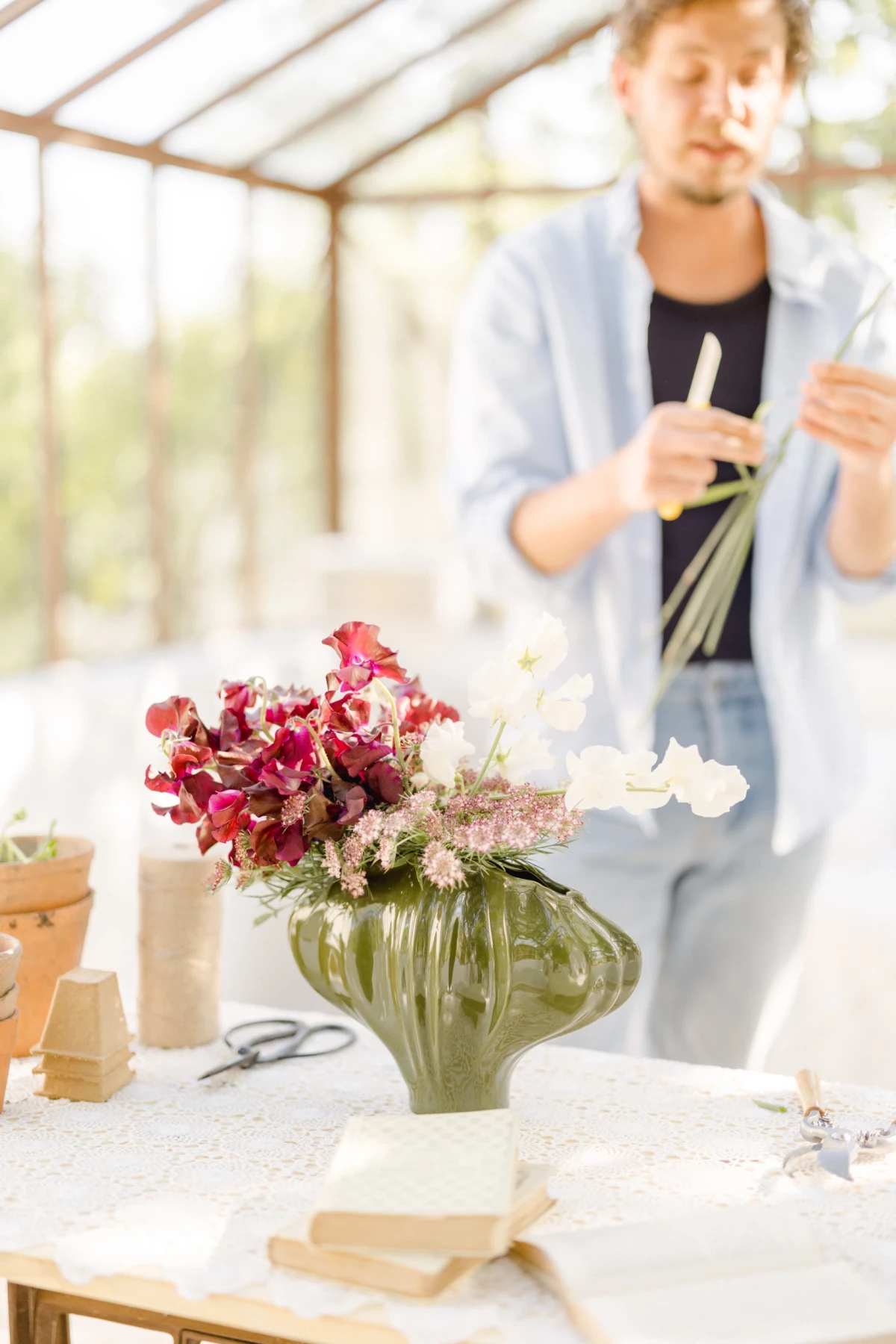Séance corporate fleuriste : artisan travaille un bouquet de fleurs rouges dans une verrière lumineuse, ambiance douce et créative