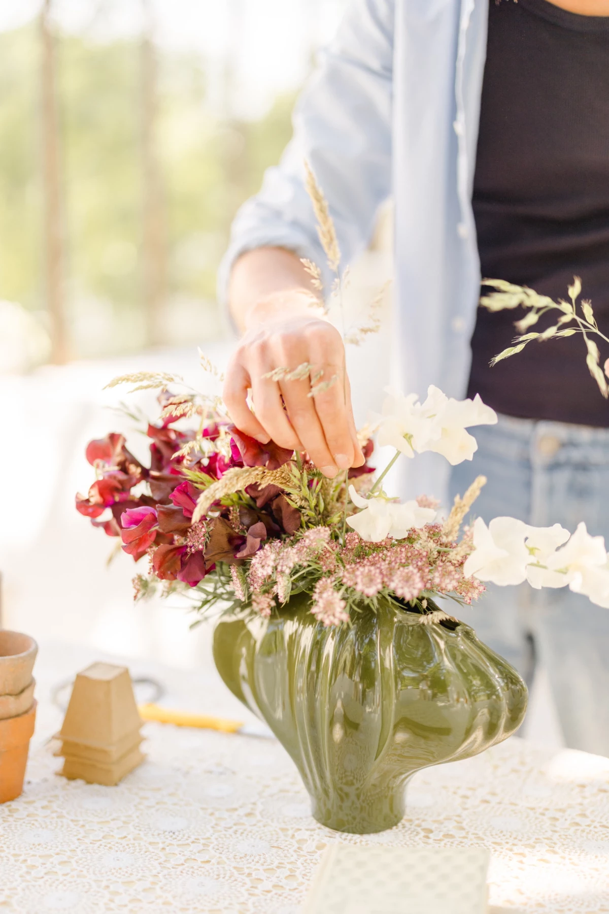 Séance corporate fleuriste : mains délicates arrangent un bouquet de fleurs dans un vase vert, geste artisanal plein de douceur