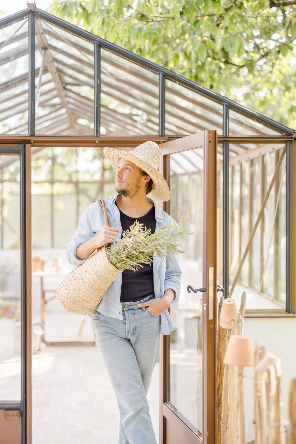 Portrait corporate fleuriste devant verrière : artisane en chapeau avec bouquet de fleurs séchées, ambiance douce et naturelle