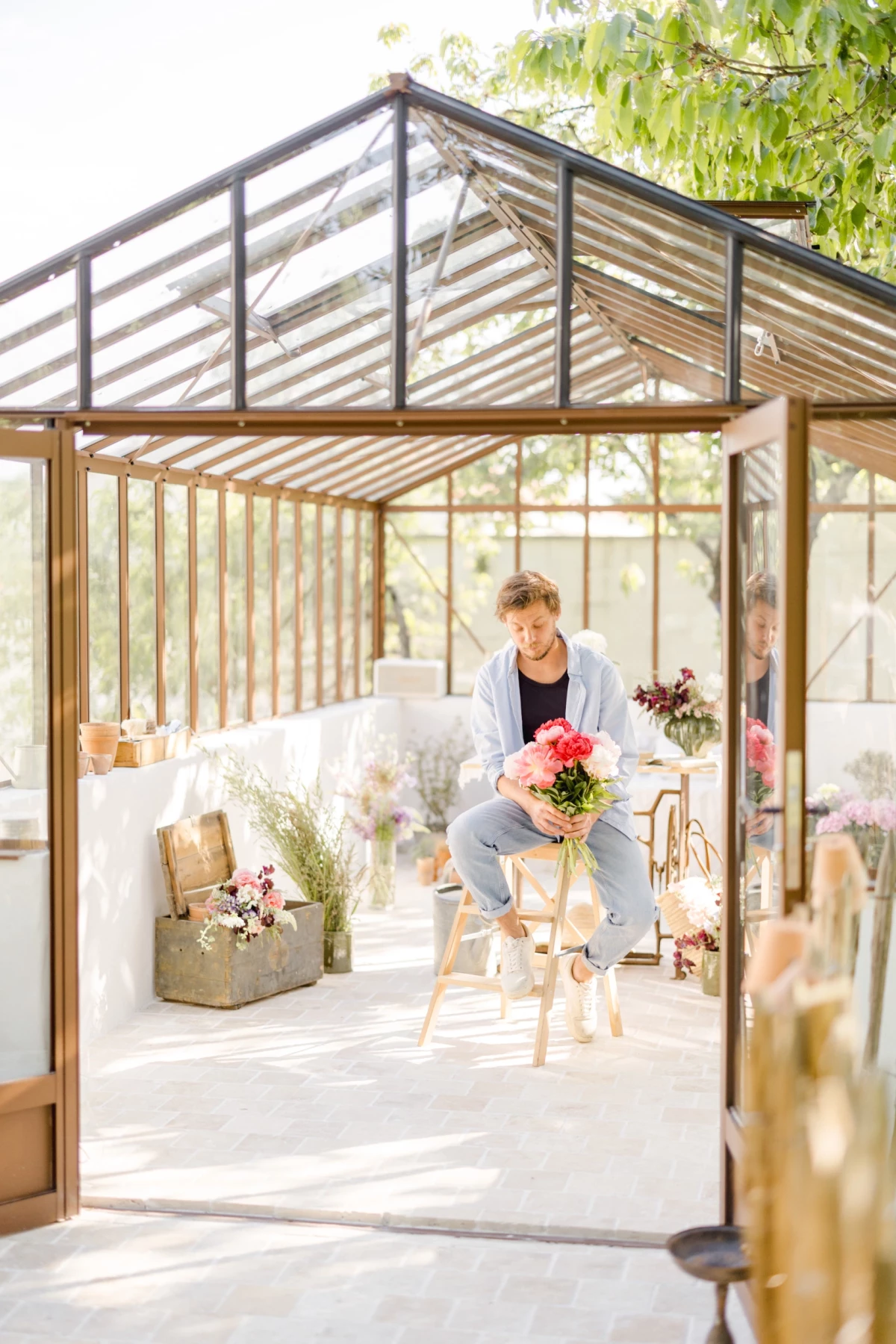 Séance corporate fleuriste : artisan au travail créant des bouquets dans une verrière lumineuse aux tons beiges et naturels