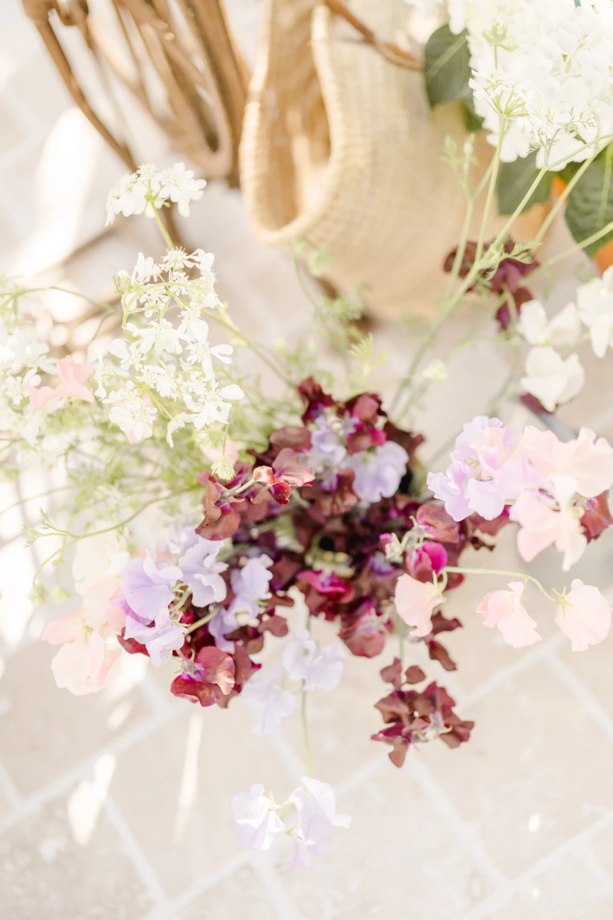 Séance corporate fleuriste : bouquet délicat de fleurs roses et bordeaux sur fond de verrière lumineuse, ambiance douce et printanière
